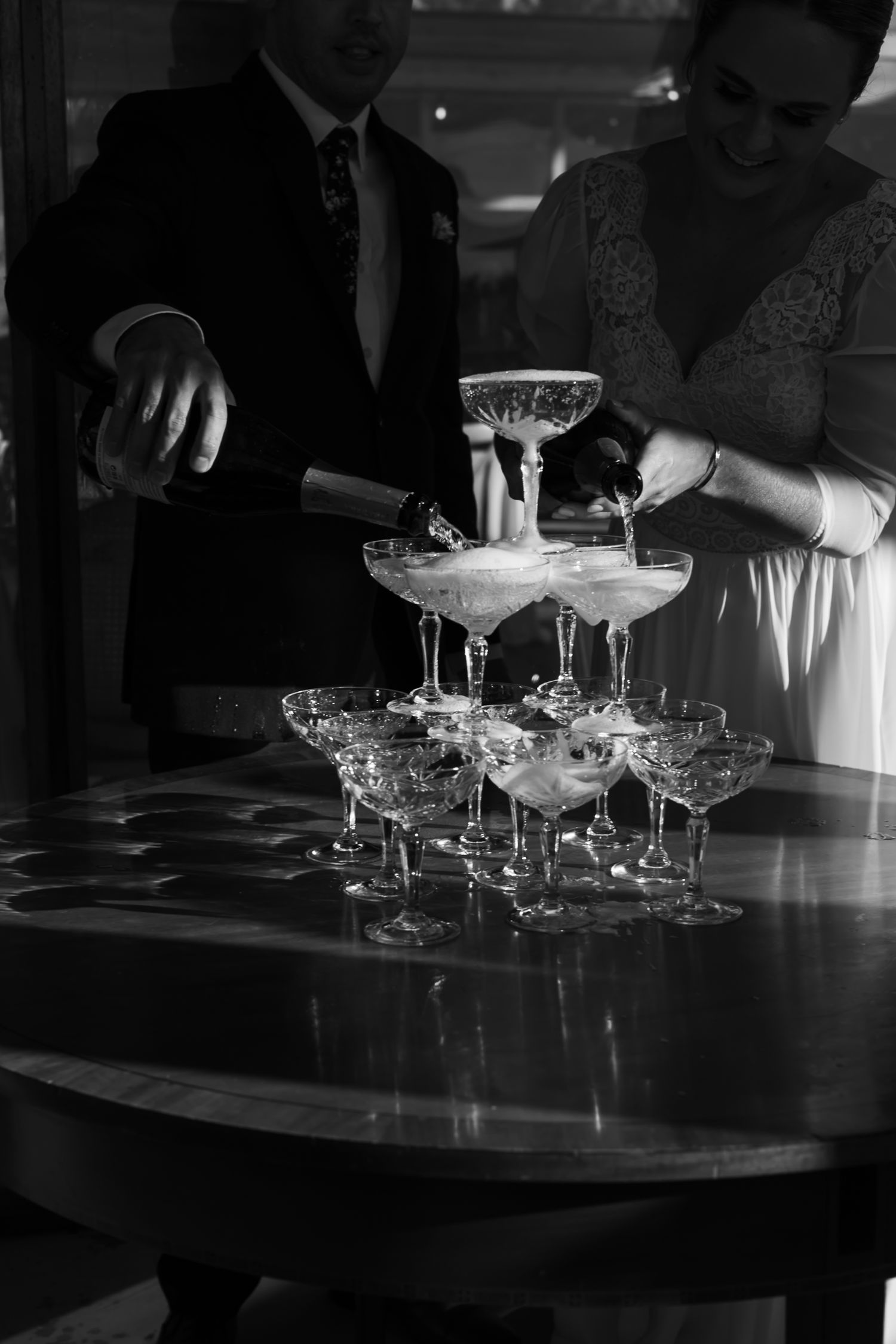 Crystal champagne glasses arranged on a dark surface in classic cocktail setup in black and white tones. Champaign tower.