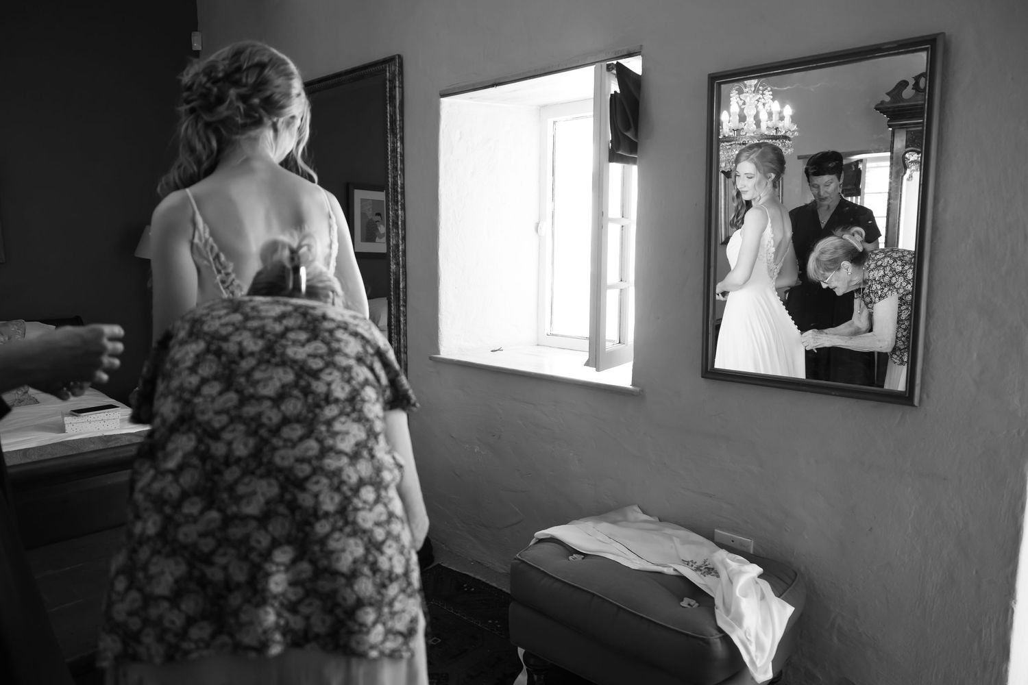 A black and white photograph showing reflections in mirrors inside a bedroom with natural window light.