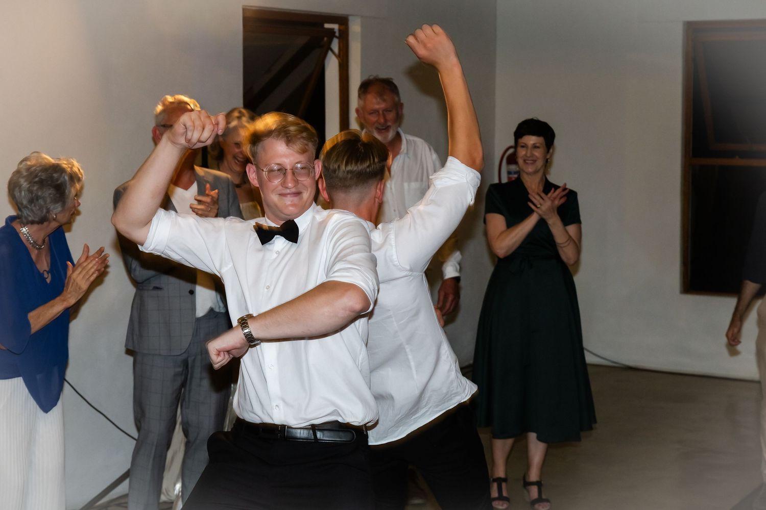 Wedding party members dancing and celebrating with raised arms on the dance floor.