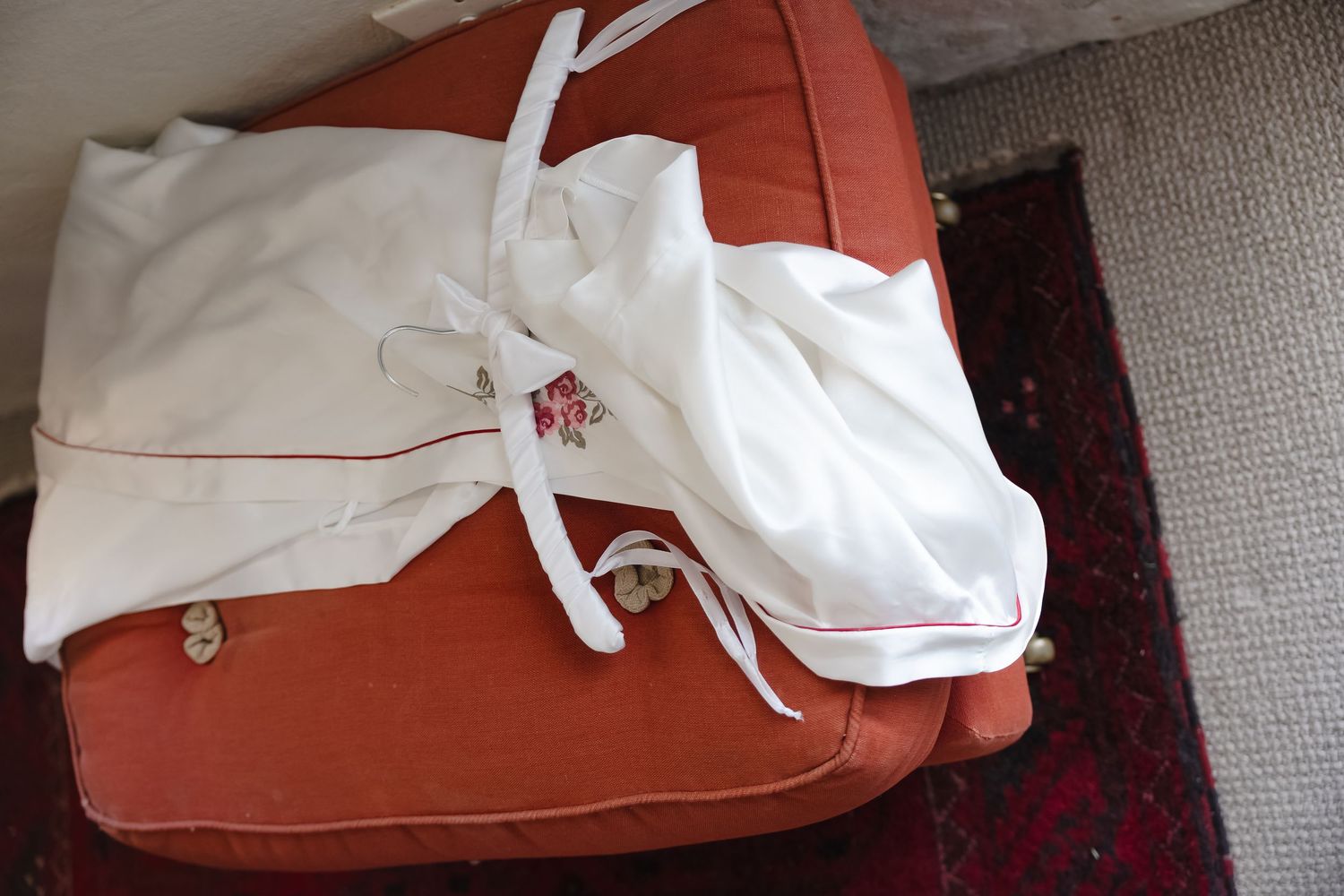 White wedding dress details laid out on a red couch cushion.