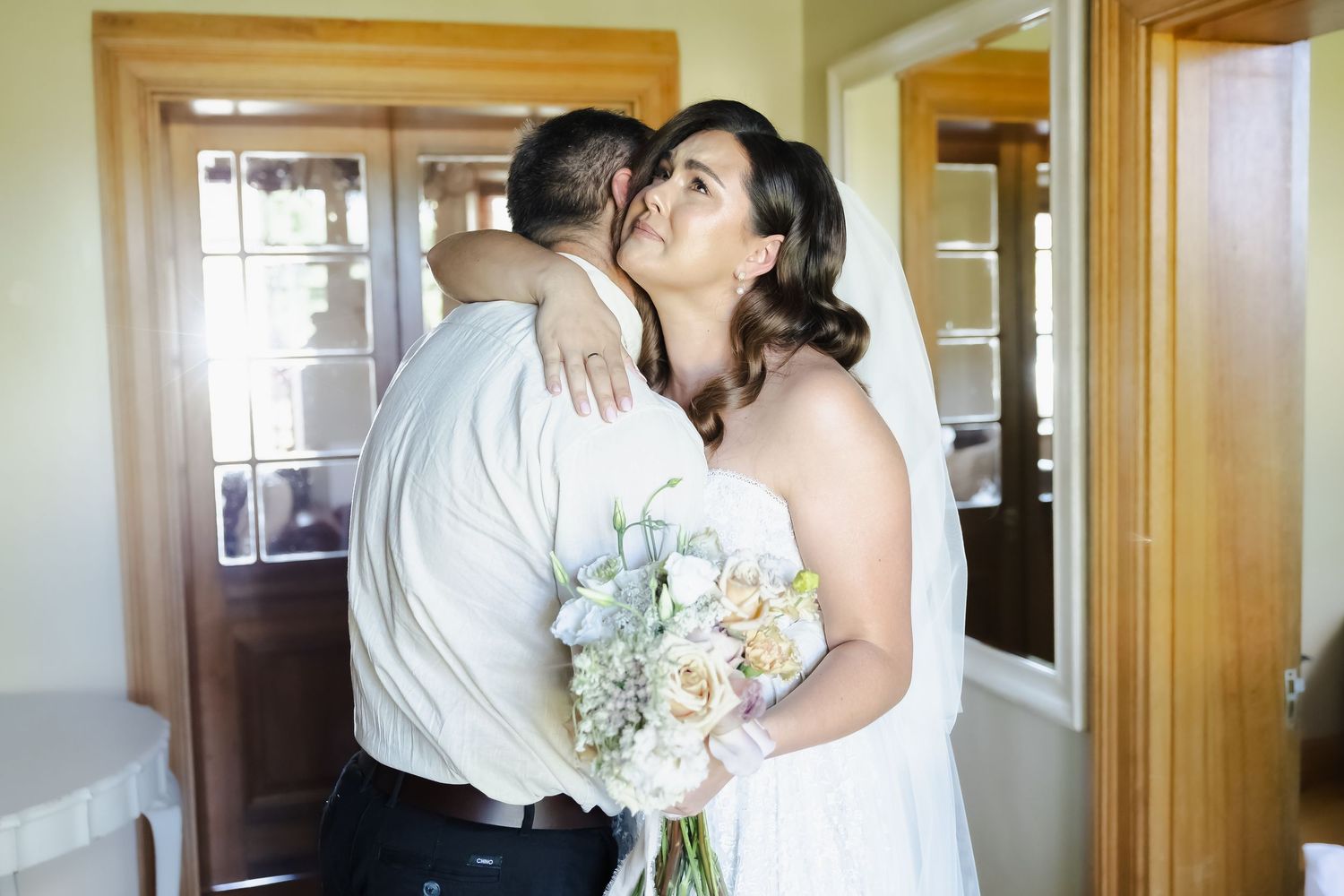 A tender embrace between a couple in wedding attire standing in a warmly lit hallway.