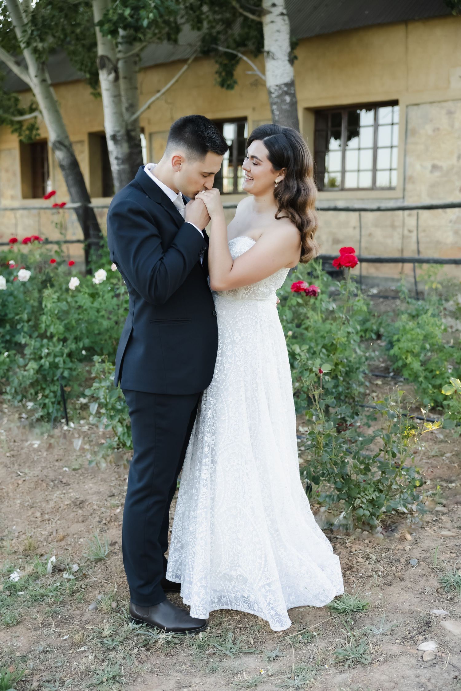 A romantic wedding photoshoot in a garden with roses as a couple shares tender moments in formal attire.