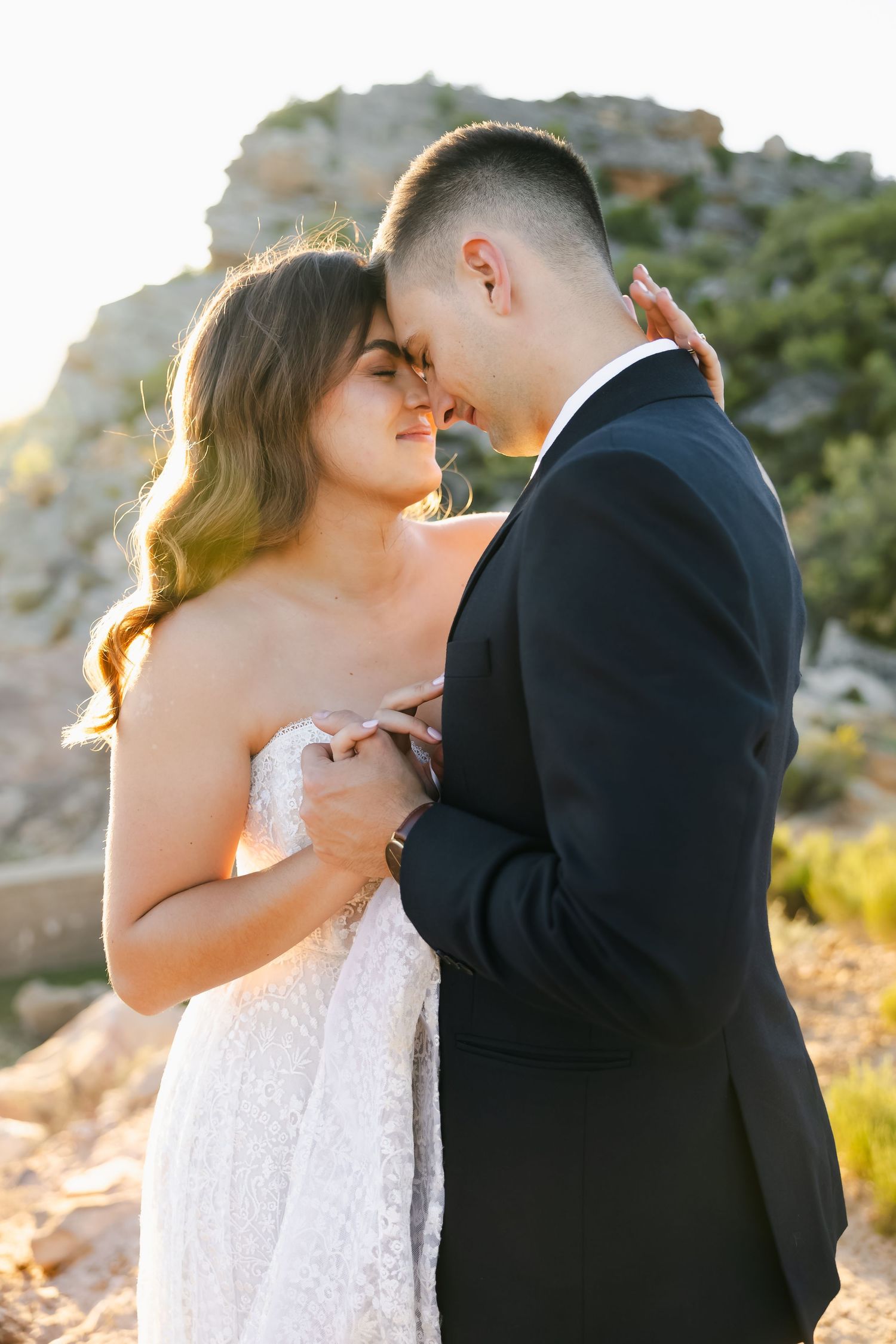 Intimate wedding photos captured on a desert hillside during sunset showing tender moments between newlyweds.