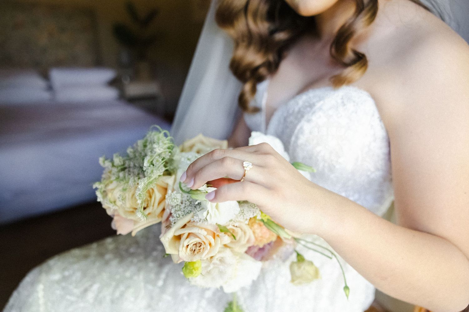 A wedding bouquet with cream roses and delicate greenery is held in soft natural lighting.