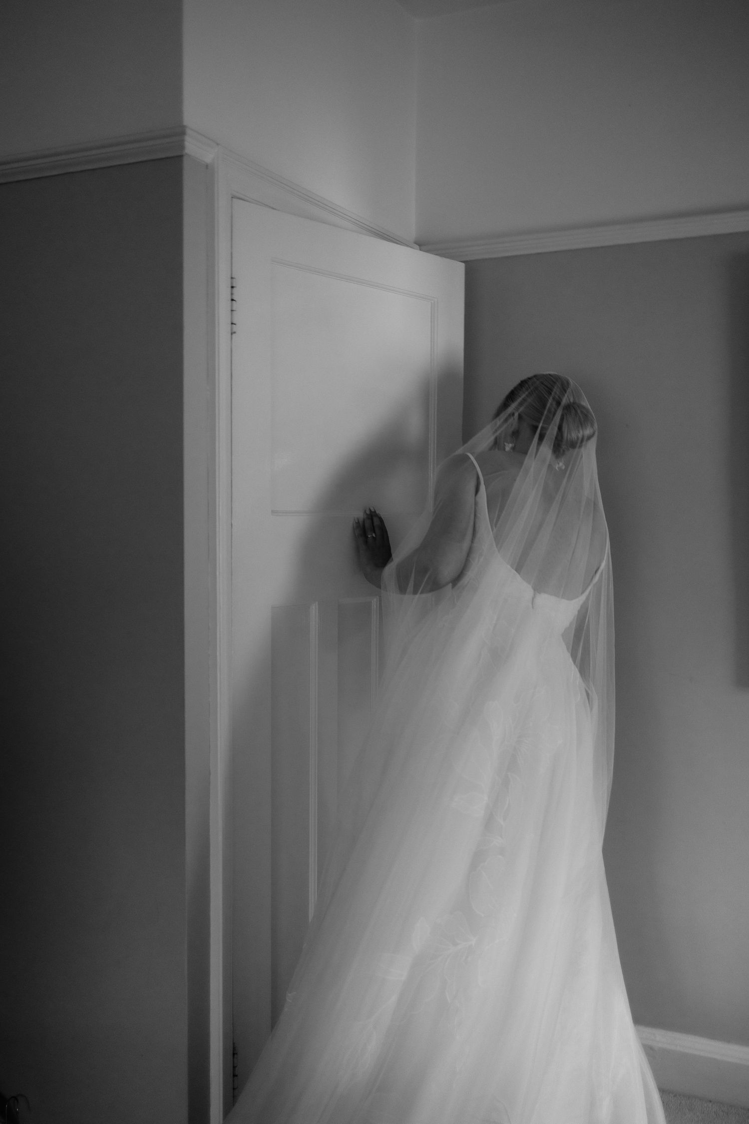 Editorial-inspired Cheshire wedding photography of bride peering through door, looking for father