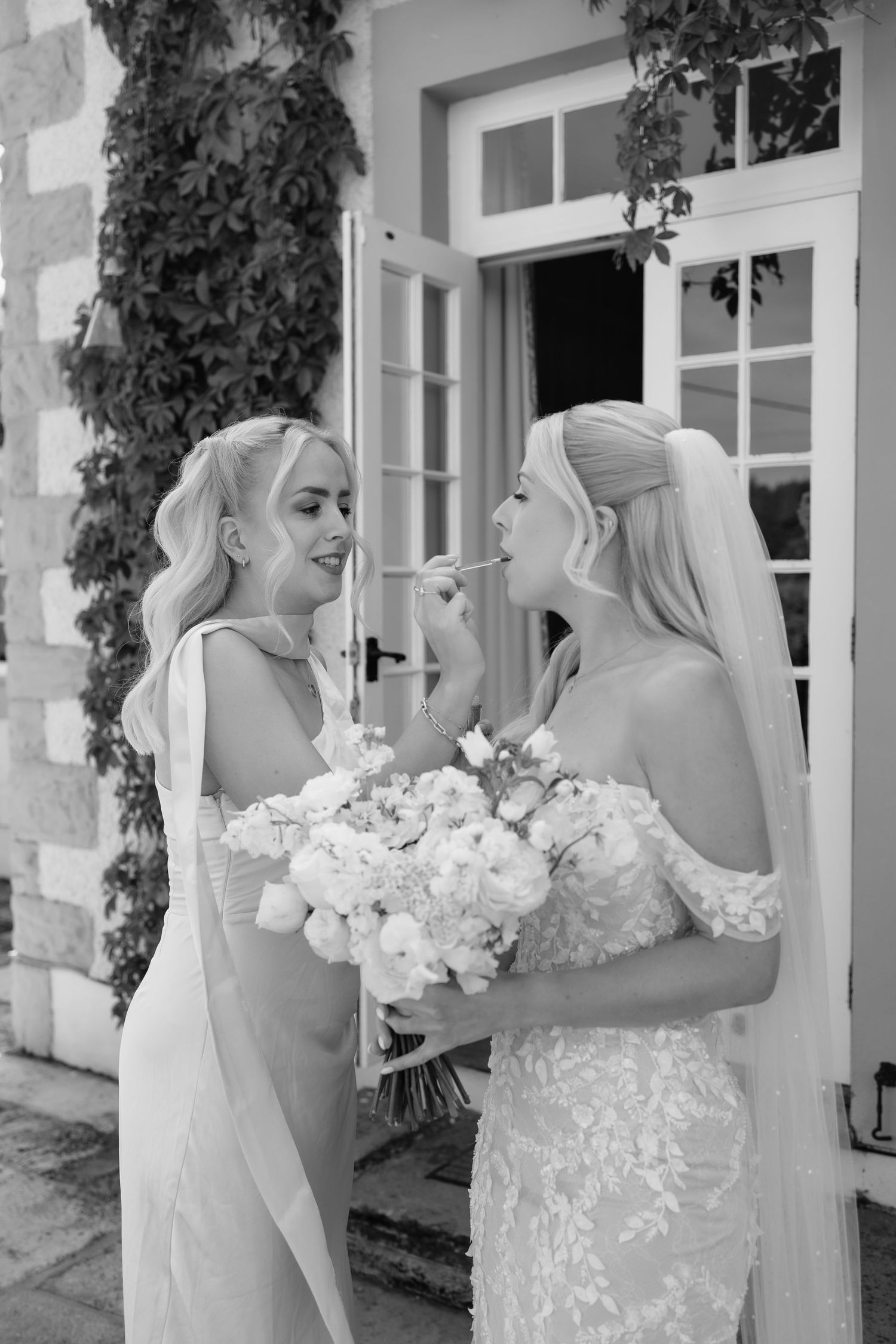bride and made of honour doing final lipstick touch ups before walking down the aisle of the Italian garden