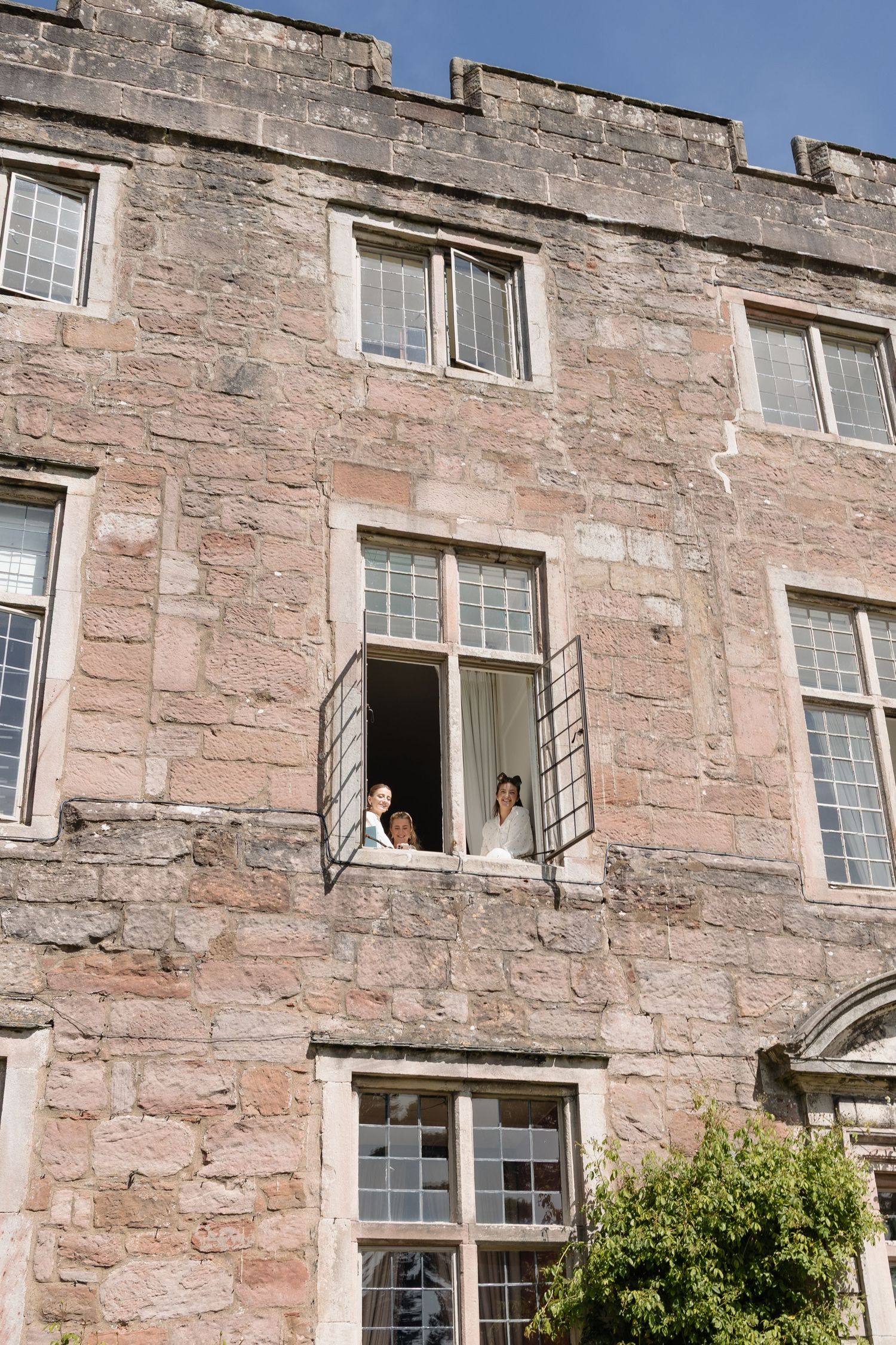 bridesmaids look down from window at Askham Hall