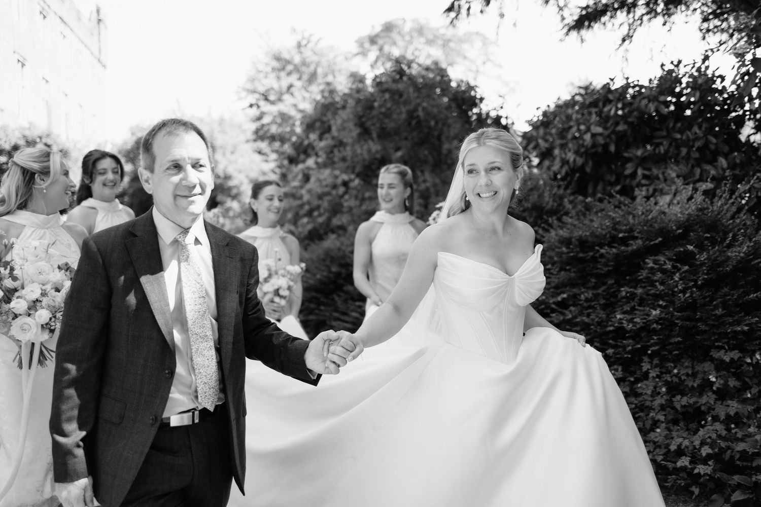 bride walking with father and bridesmaids to church ceremony, during Askham Hall wedding