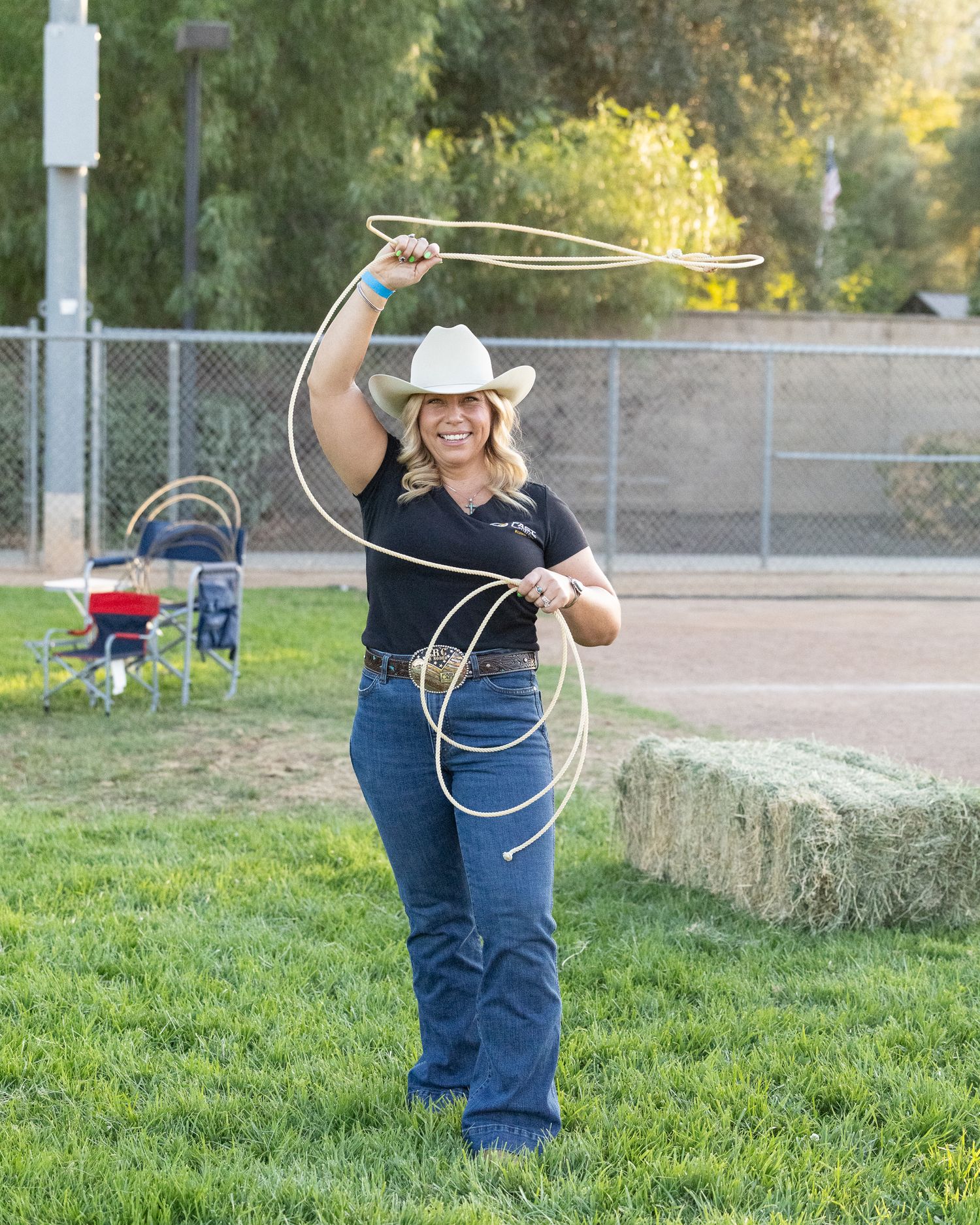 Woman in cowboy hat twirling a lasso rope outdoors on green grass at a rodeo event.