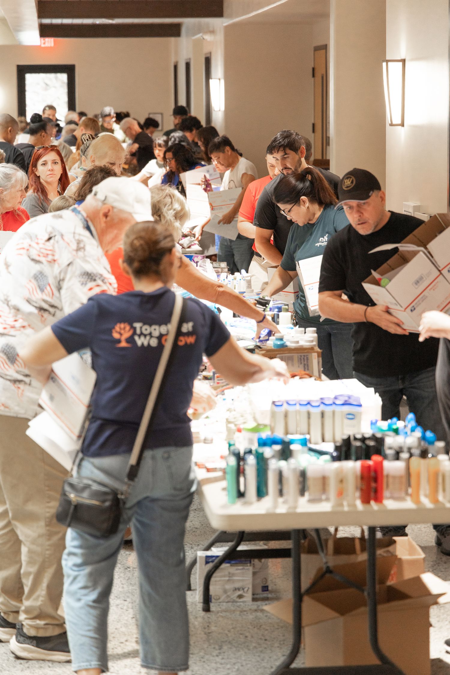 Volunteers sorting donations at long tables during a community relief event, with a woman wearing a Together We Grow shirt.