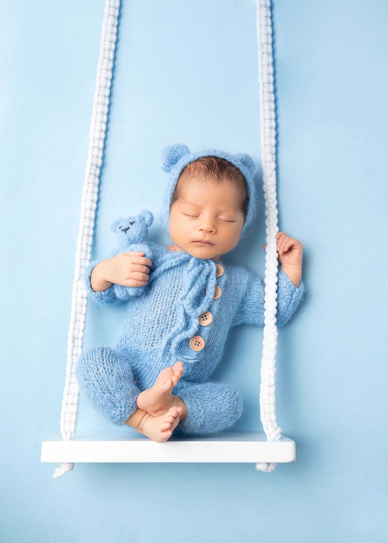 Newborn photoshoot in Gravesend Kent with baby in blue outfit lying on small swing prop in studio