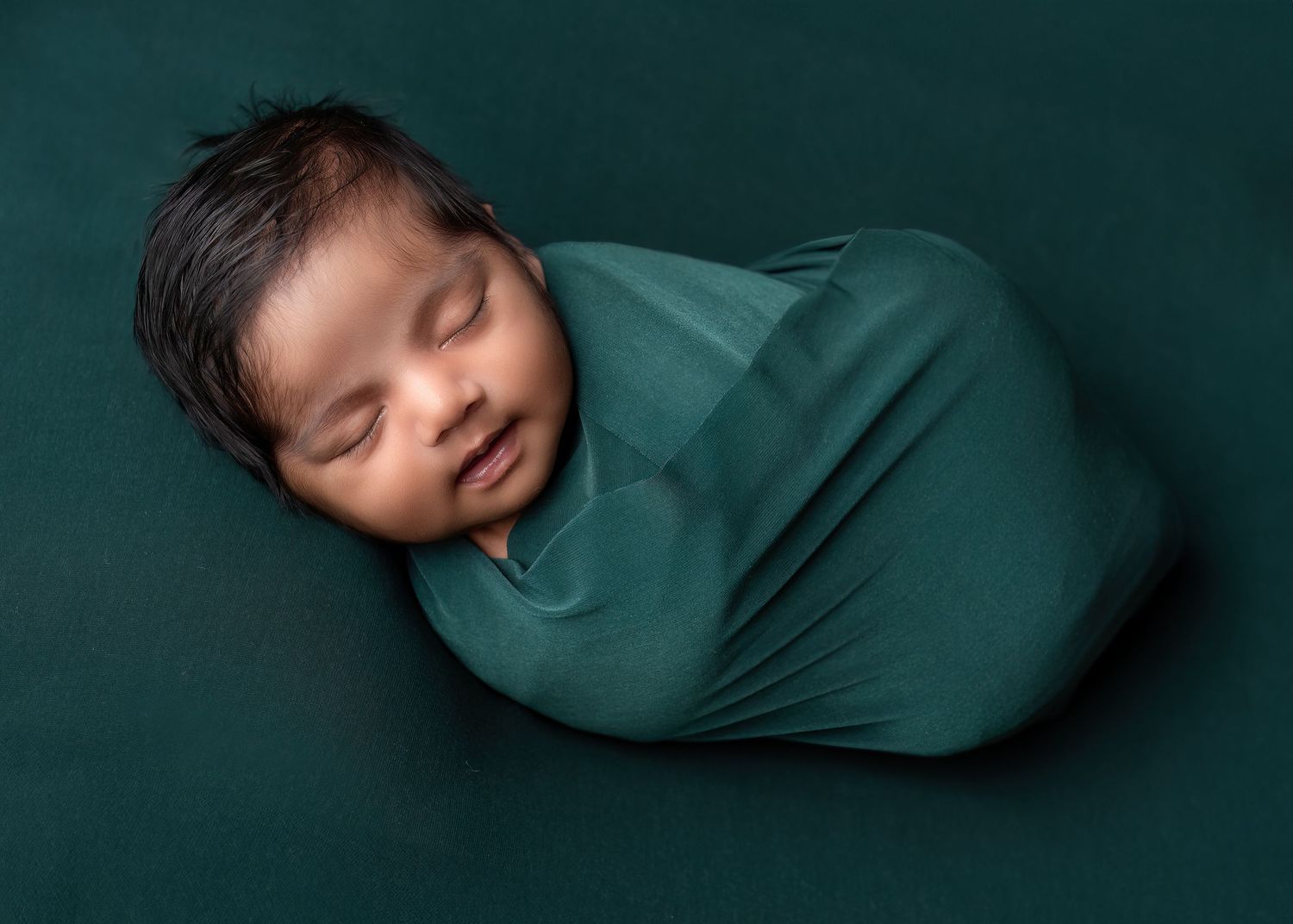 Newborn photography in Gravesend Kent with baby wrapped in green swaddle sleeping in studio