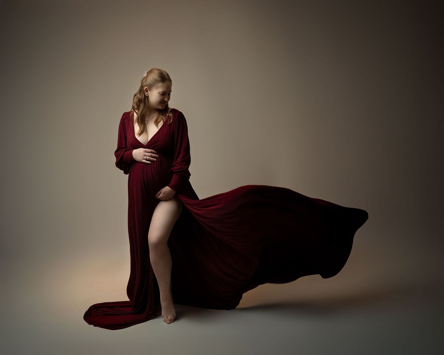 Maternity photography session in Gravesend Kent with pregnant woman in red gown posing in studio with flowing fabric