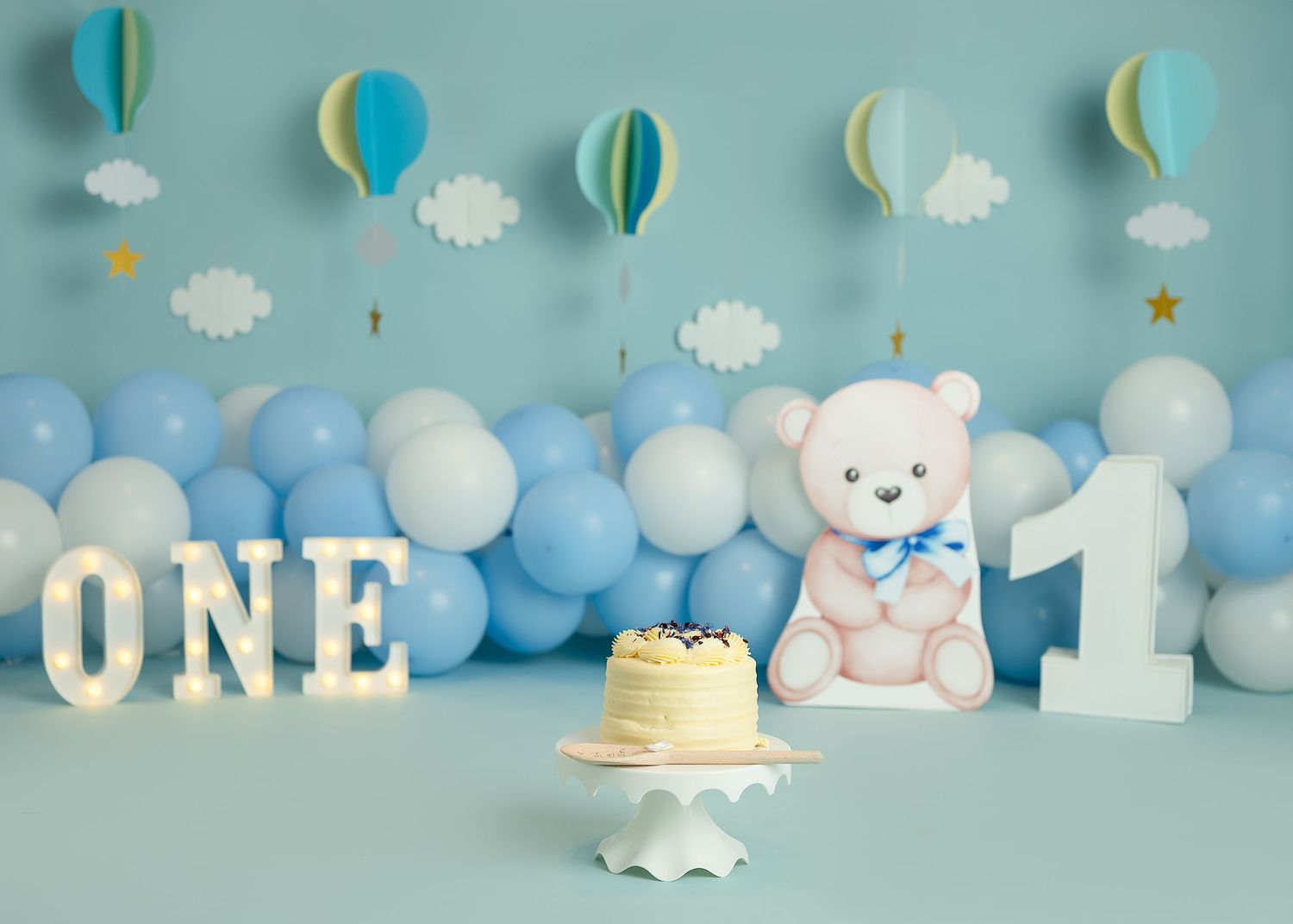 Cake smash photoshoot in Gravesend Kent with blue balloon setup and teddy bear first birthday theme