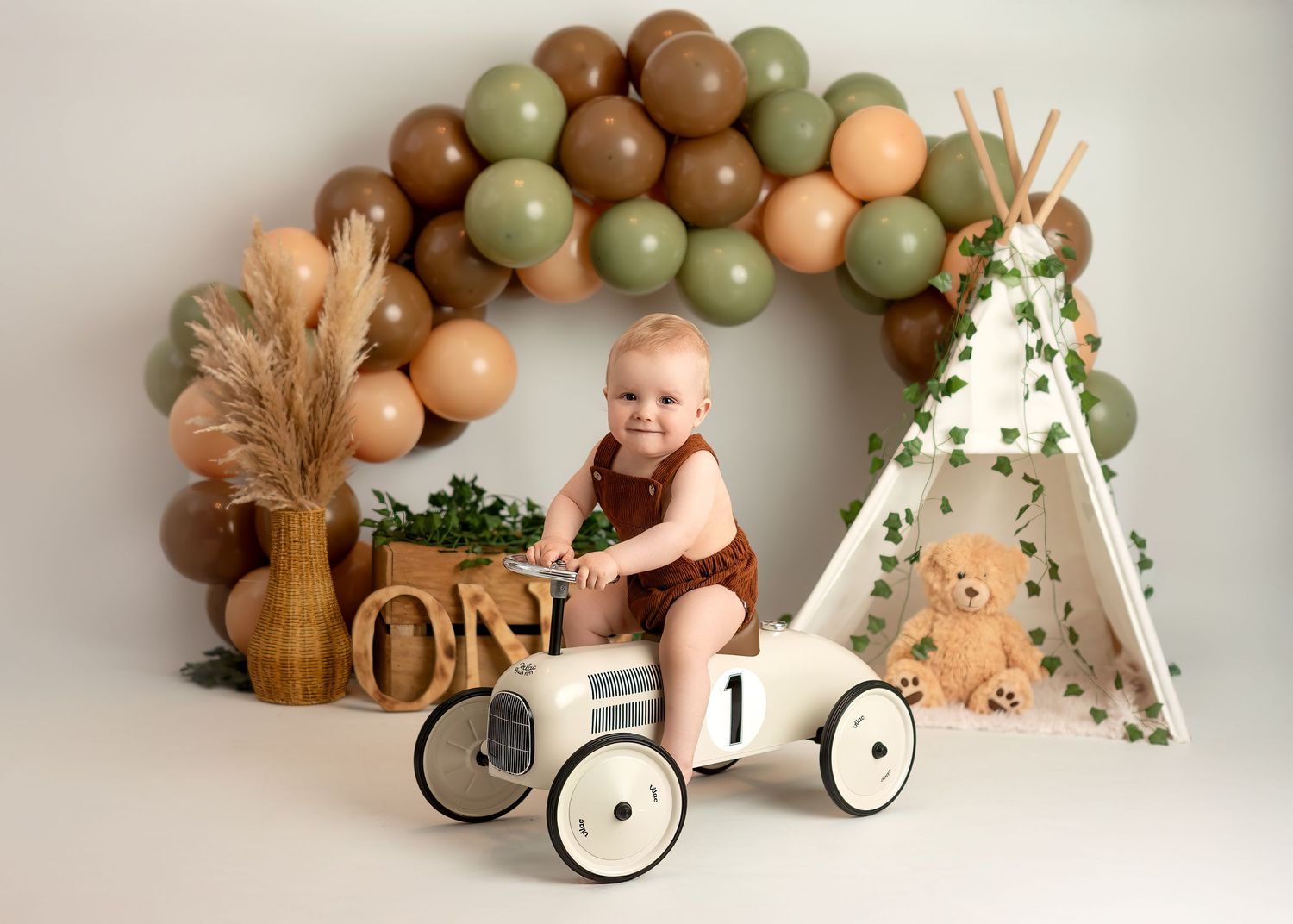 Cake smash photography session in Gravesend Kent with baby sitting on toy car with neutral balloon arch setup