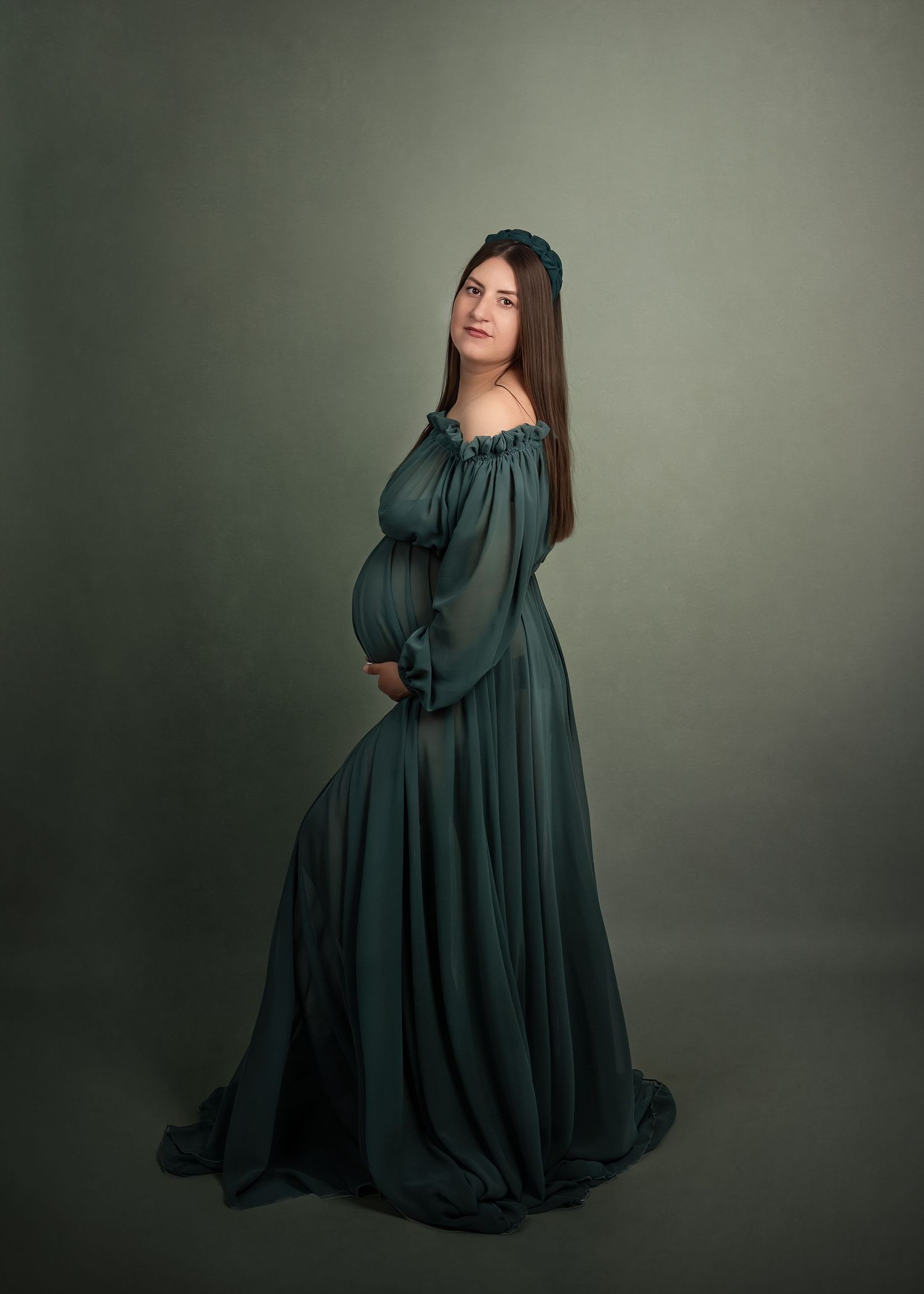 Maternity photoshoot in Gravesend Kent with pregnant woman in dark green gown posing sideways in studio