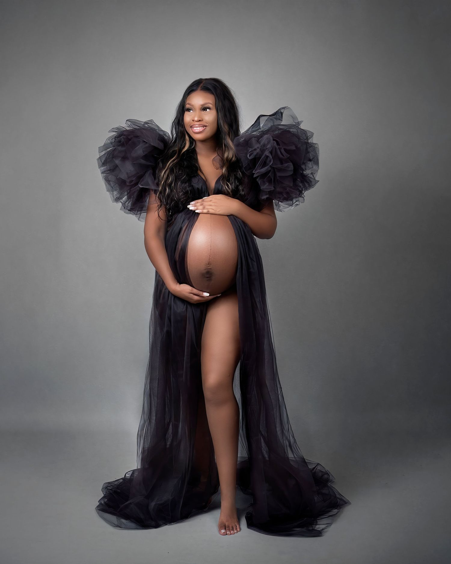 Maternity photography session in Gravesend Kent with pregnant woman in black gown with dramatic feather sleeves in studio