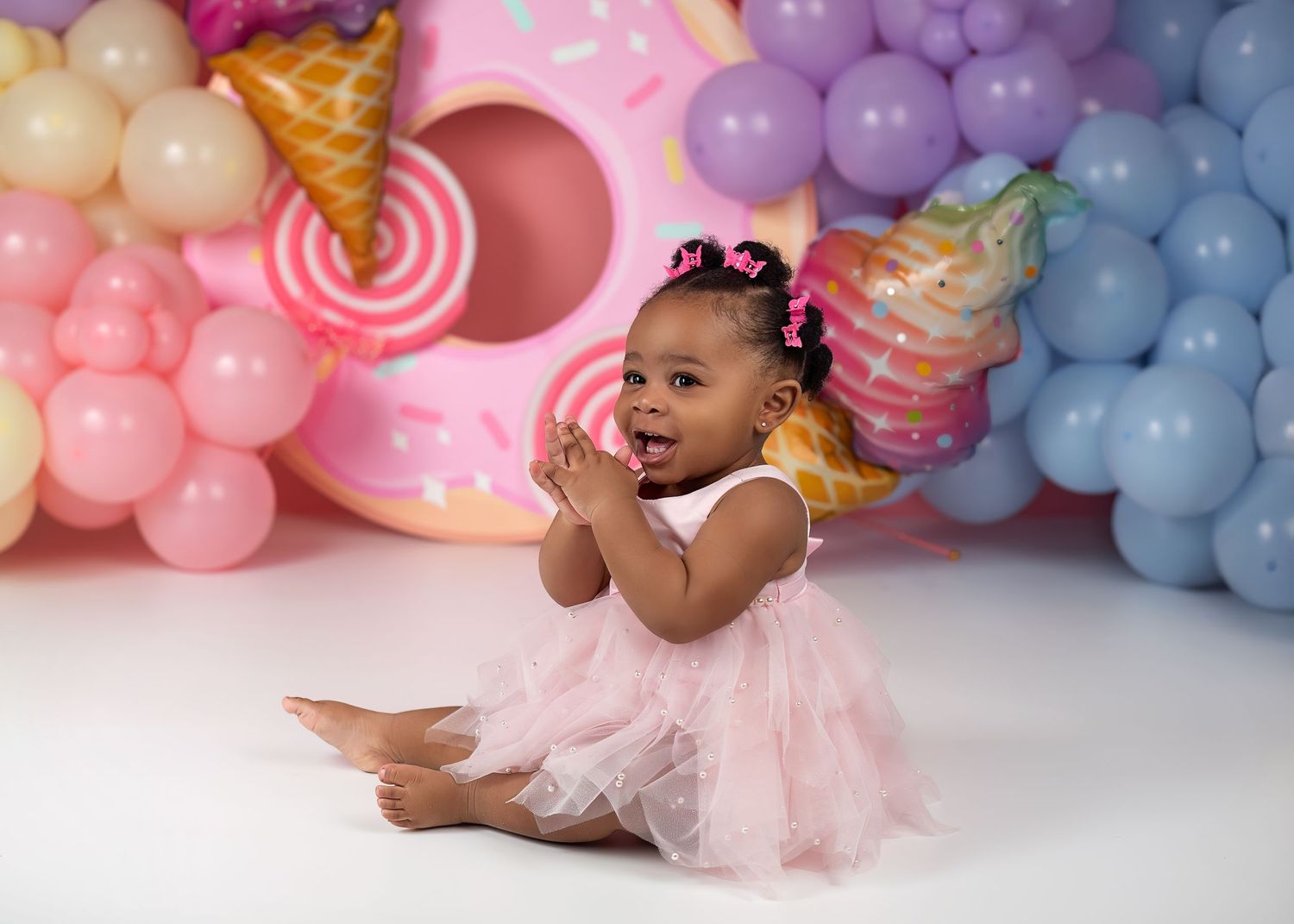 Cake smash photography session in Gravesend Kent with baby girl in pink dress with colourful balloon background