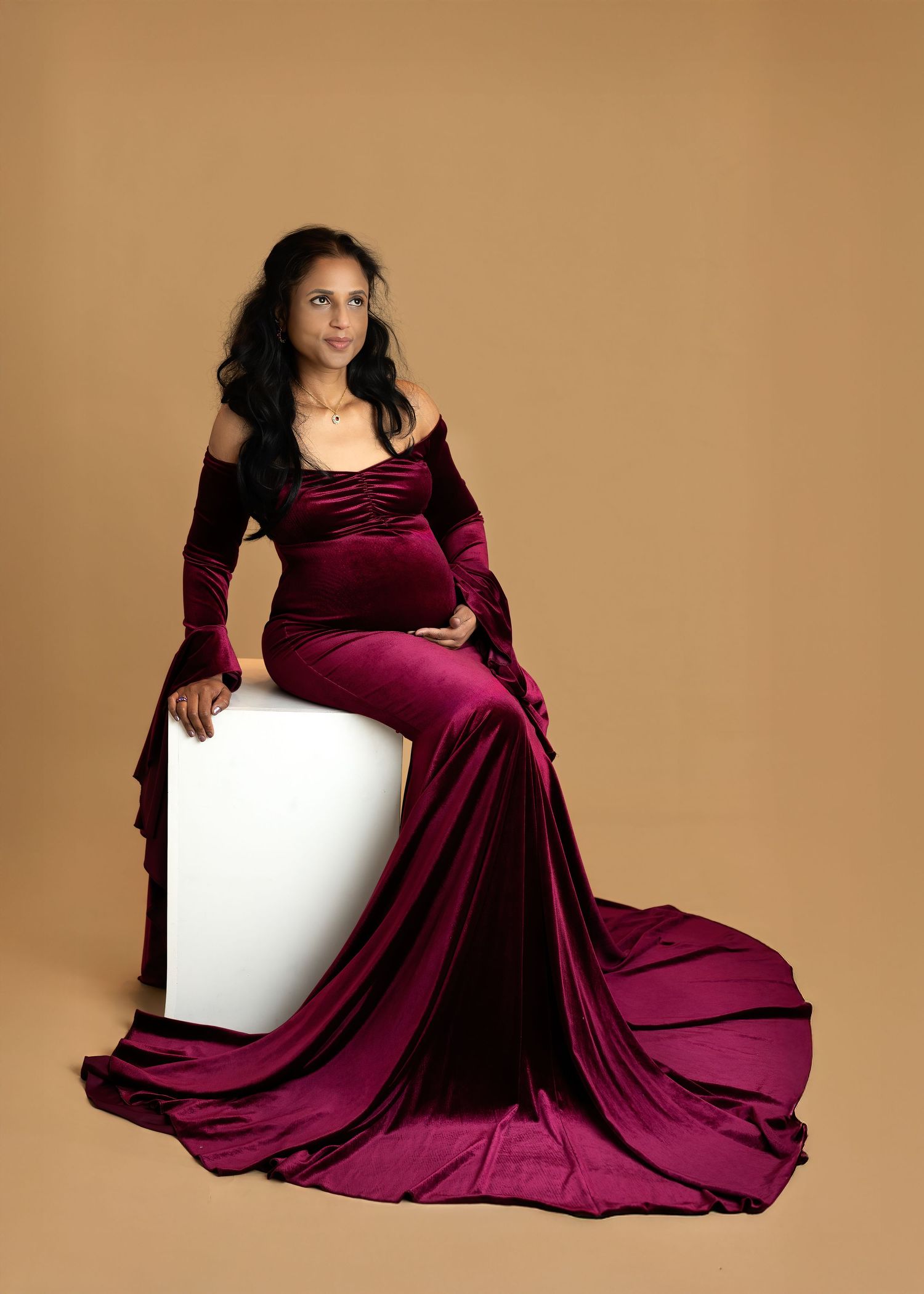 Maternity photoshoot in Gravesend Kent with pregnant woman in elegant burgundy dress sitting in studio