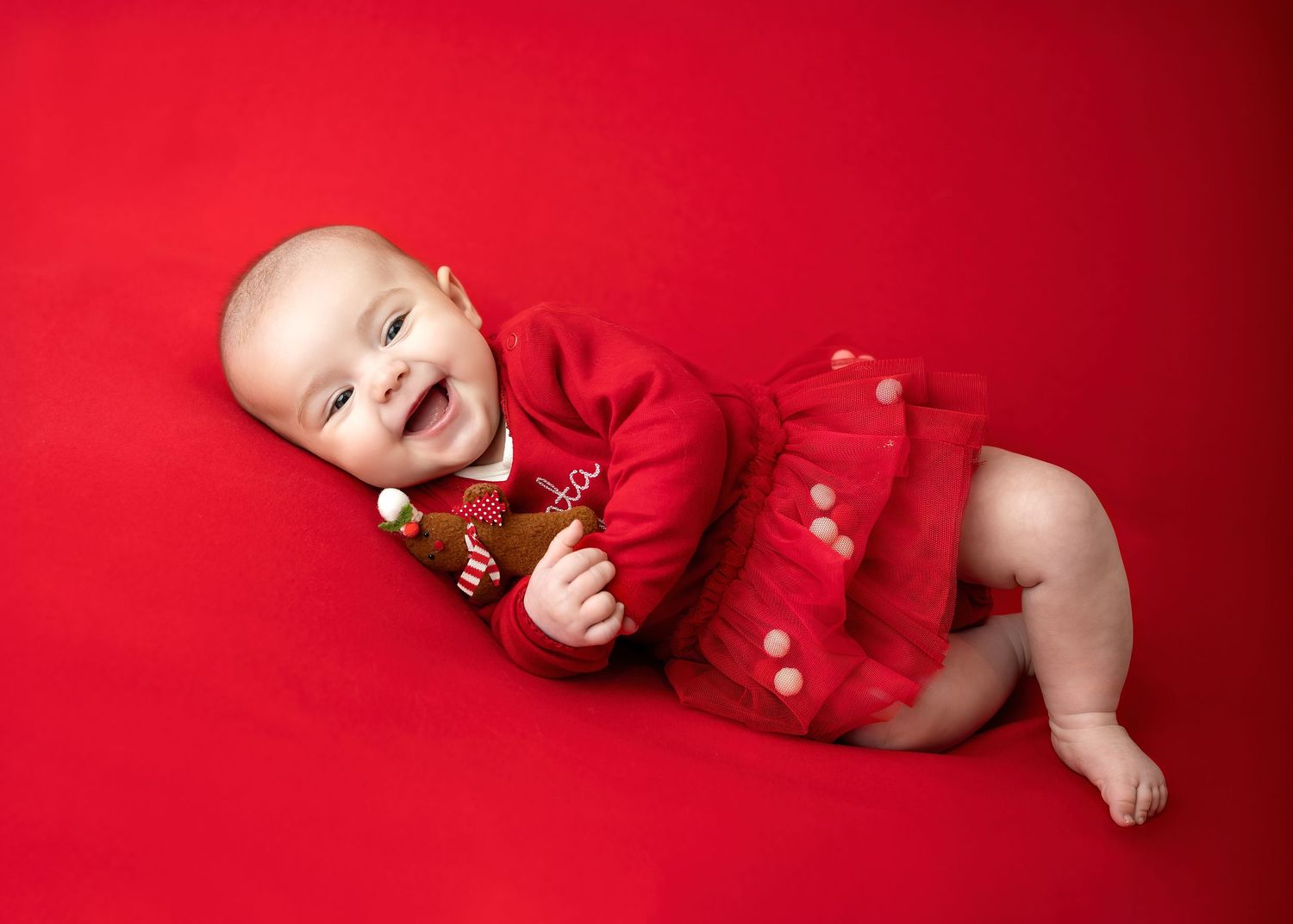 Newborn photography session in Gravesend Kent with baby wearing red outfit lying on red background in studio