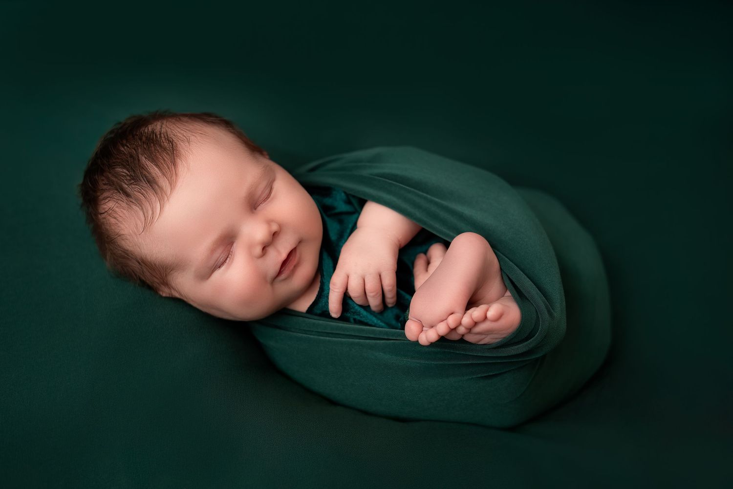 Newborn photoshoot in Gravesend Kent with baby wrapped in green fabric sleeping on dark background
