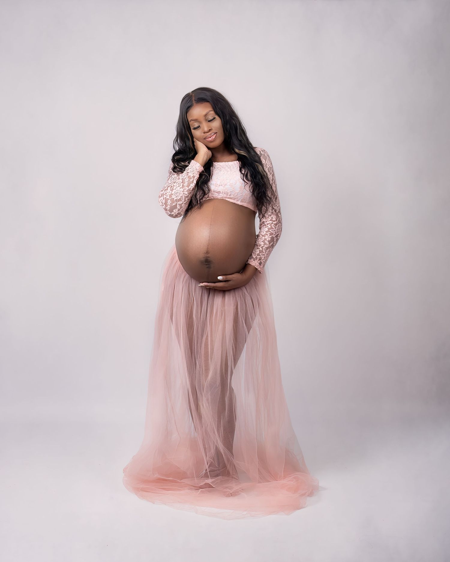Maternity photoshoot in Gravesend Kent with pregnant woman in soft pink dress holding baby bump in studio