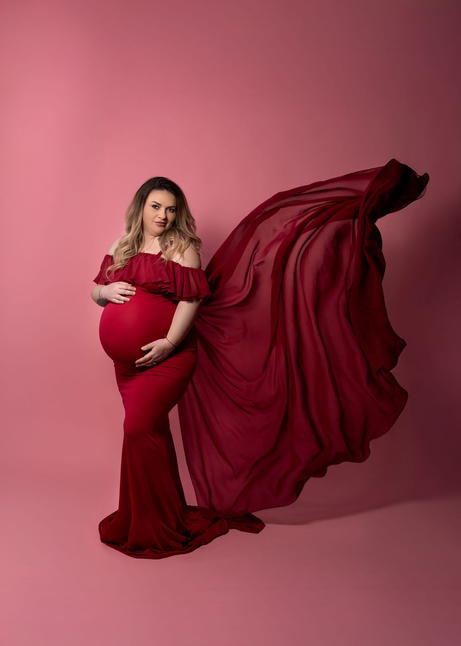 Maternity photoshoot in Gravesend Kent with pregnant woman in red flowing gown on pink background