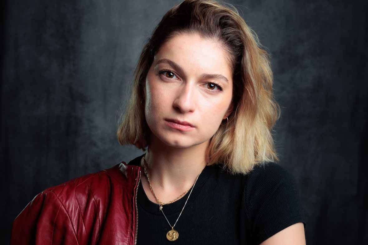 Creative headshot of blonde woman in red leather and gold layered necklaces