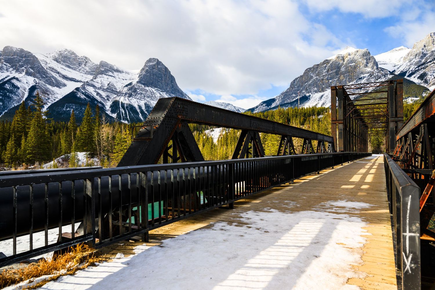 Snow-dusted bridge leads to Rocky Mountain peaks in Canmore, Alberta, Canada on a partly cloudy winter day.