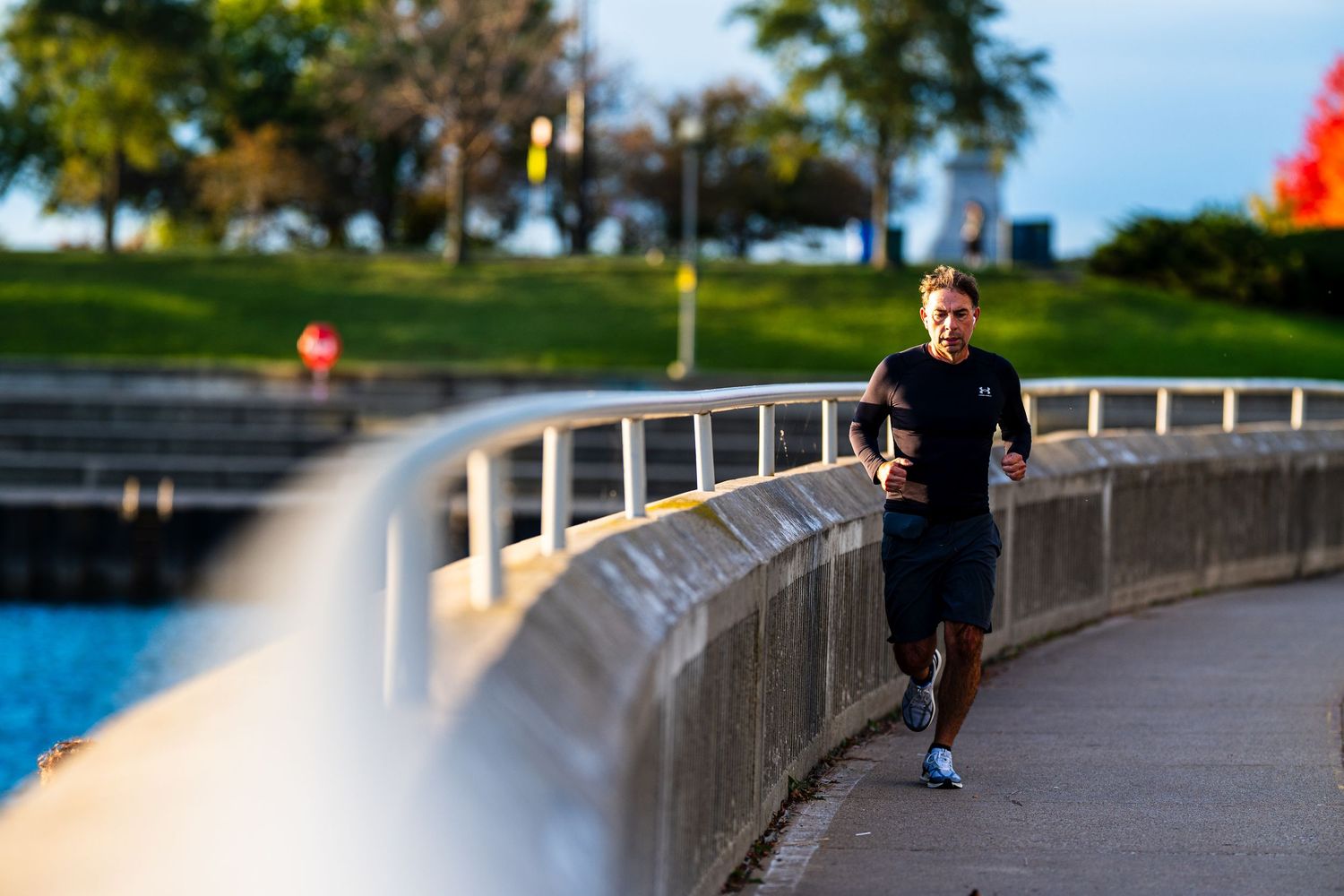 Man jogging along a scenic waterfront path in a park during golden hour, wearing black athletic wear.
