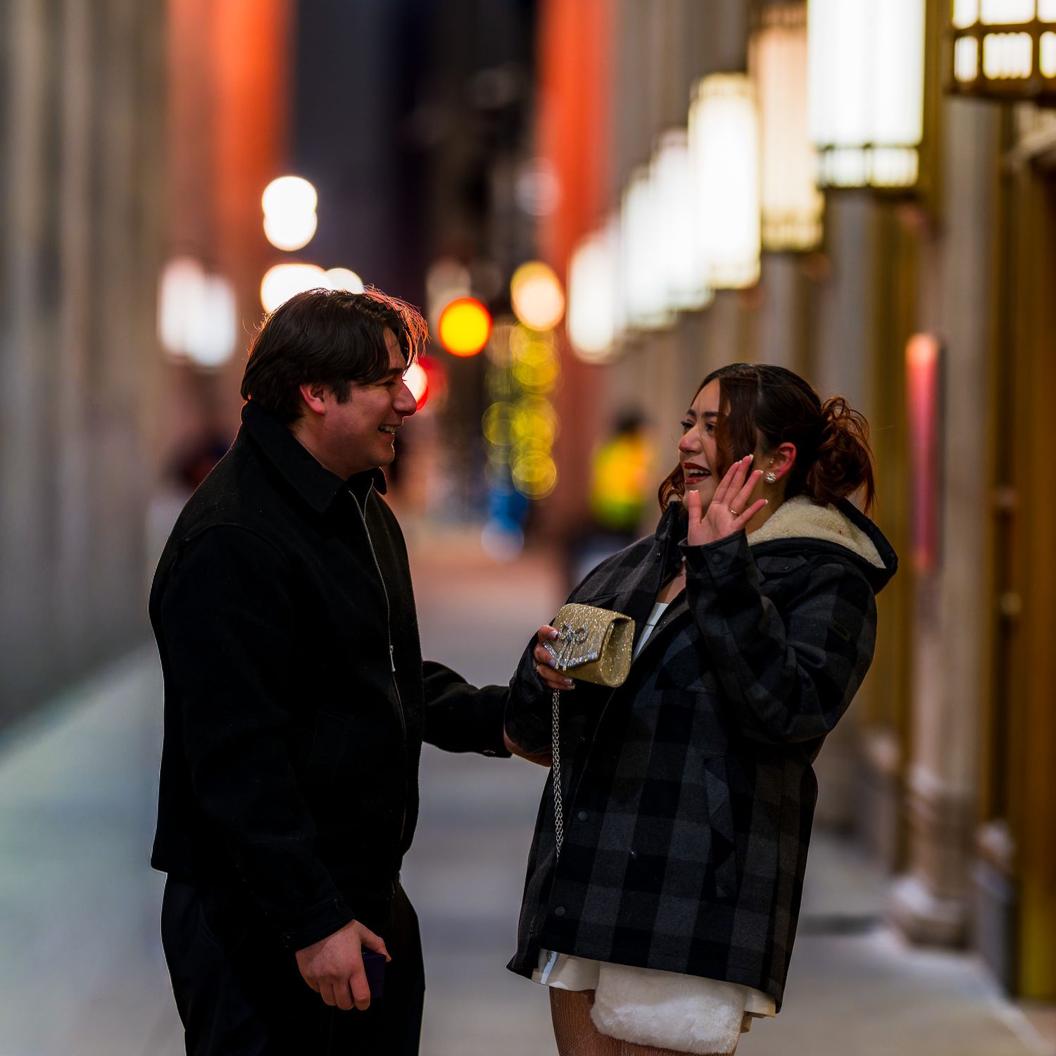 Couple talking on a city street at night, surrounded by glowing lights and urban architecture.