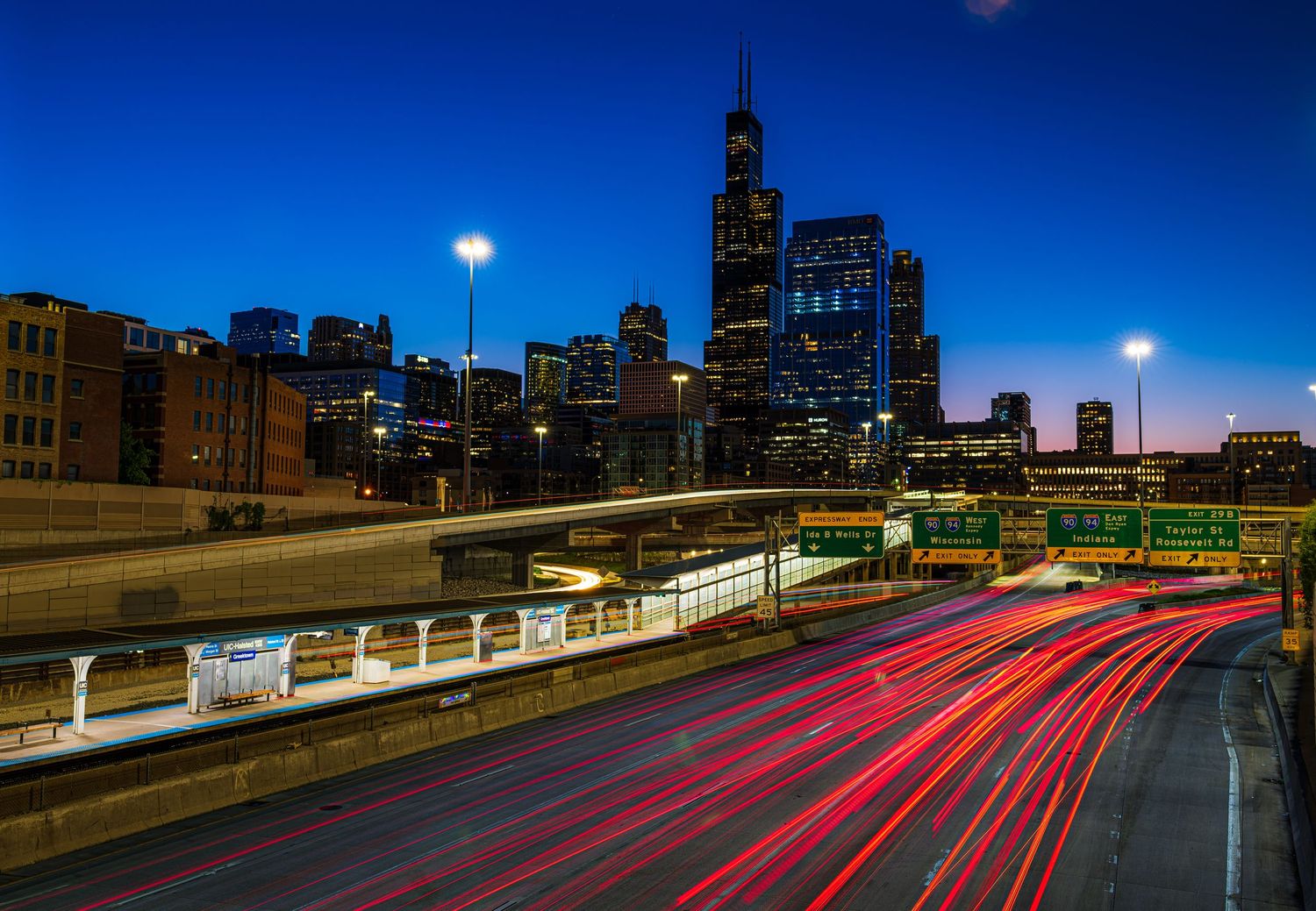 Long exposure shot of Chicago highway traffic light trails at dusk with city skyline and Willis Tower in background.