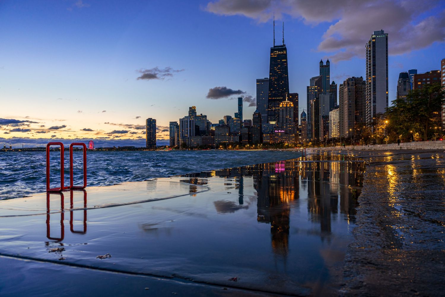 Chicago skyline reflecting in Lake Michigan at dusk with city lights and dramatic blue sky.