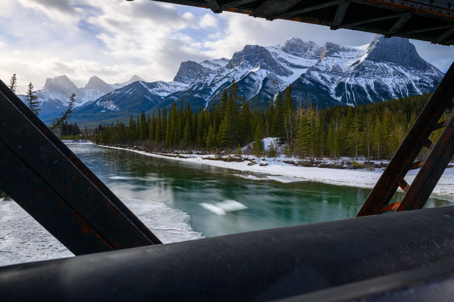 Snow-capped Rocky Mountains viewed through a covered bridge frame over a turquoise river in Canmore, Alberta, Canada.