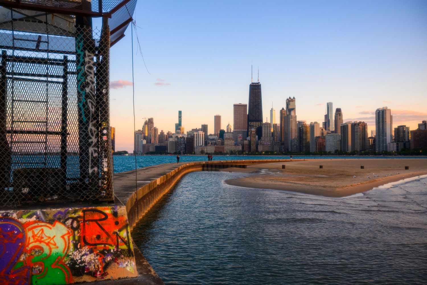 Chicago skyline at sunset viewed from North Avenue Beach with colorful graffiti and calm Lake Michigan waters.