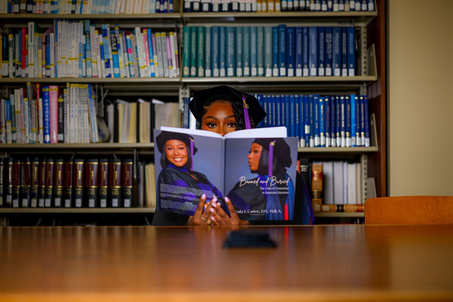 Young woman reading a book titled 'Bound and Buried' at a library table with bookshelves in the background.