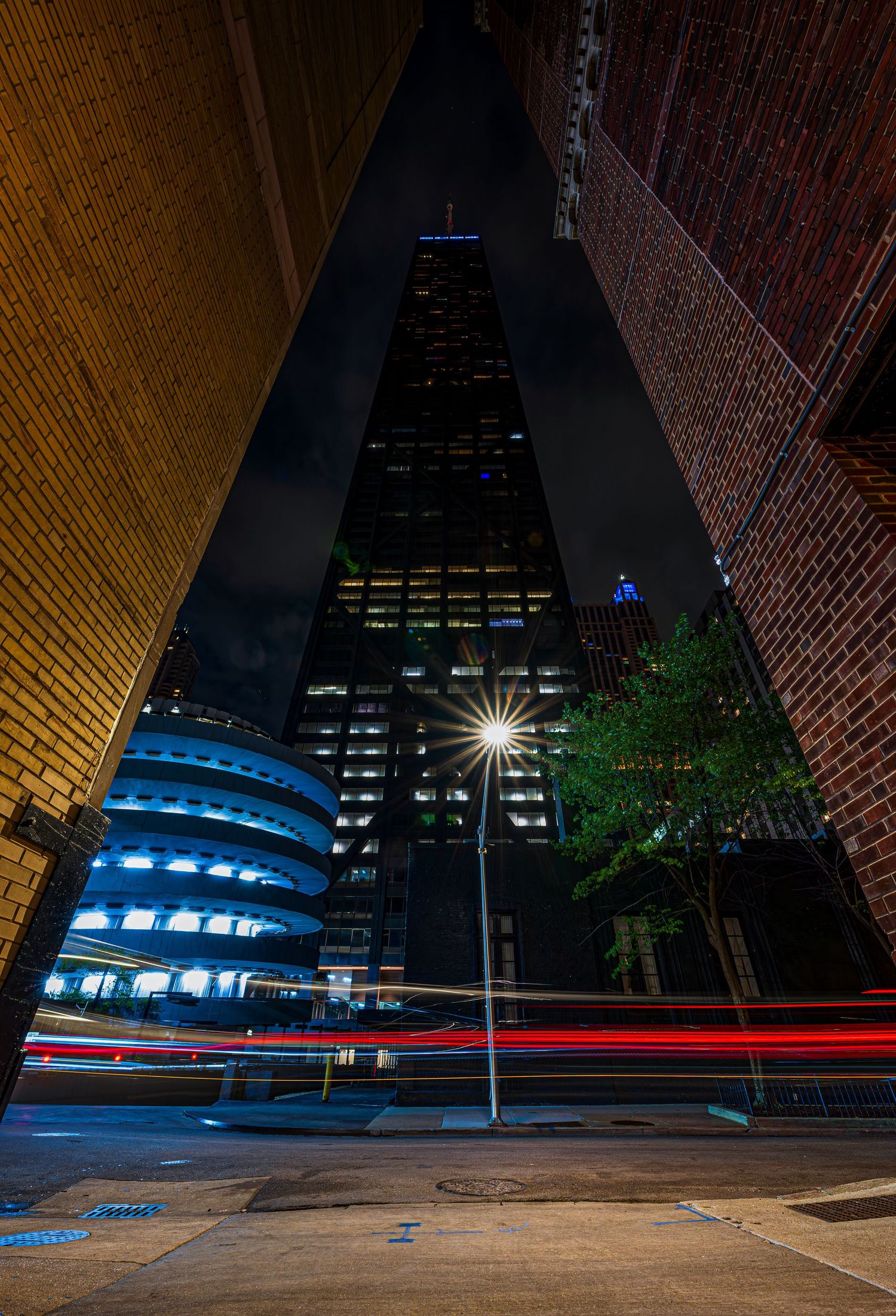 Night cityscape with light trails from traffic between buildings, framing a towering skyscraper illuminated against the dark sky.