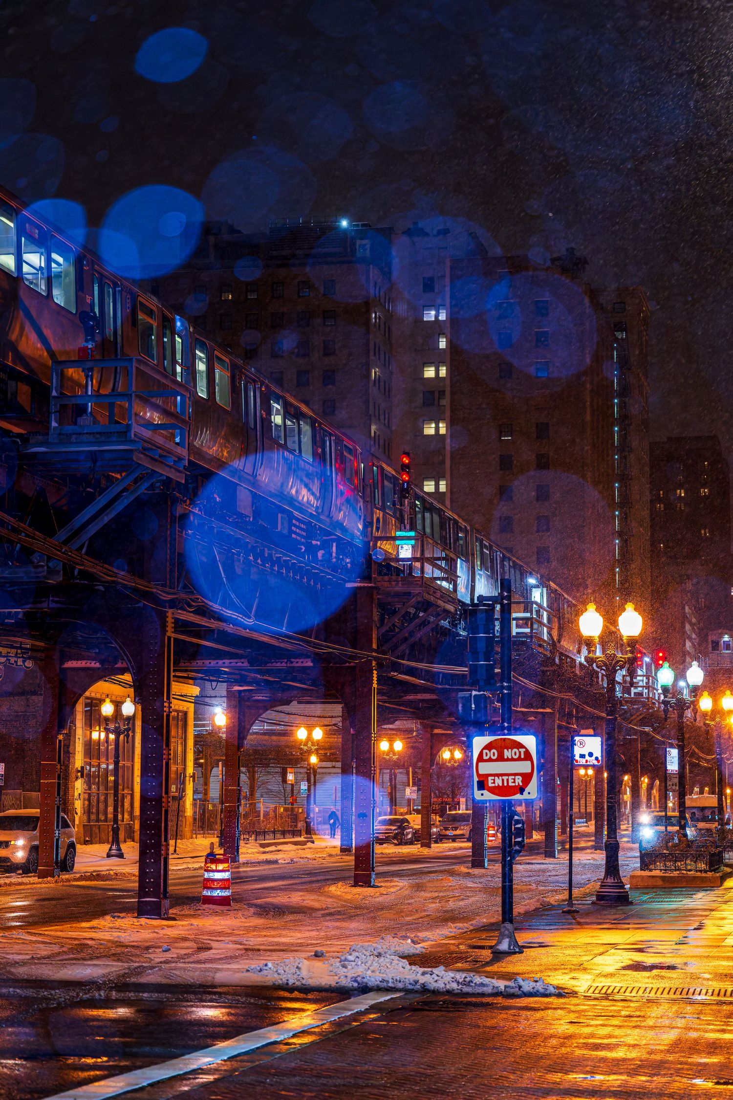 Chicago elevated train at night with glowing street lamps, wet streets, and bokeh light effects in a moody urban scene.