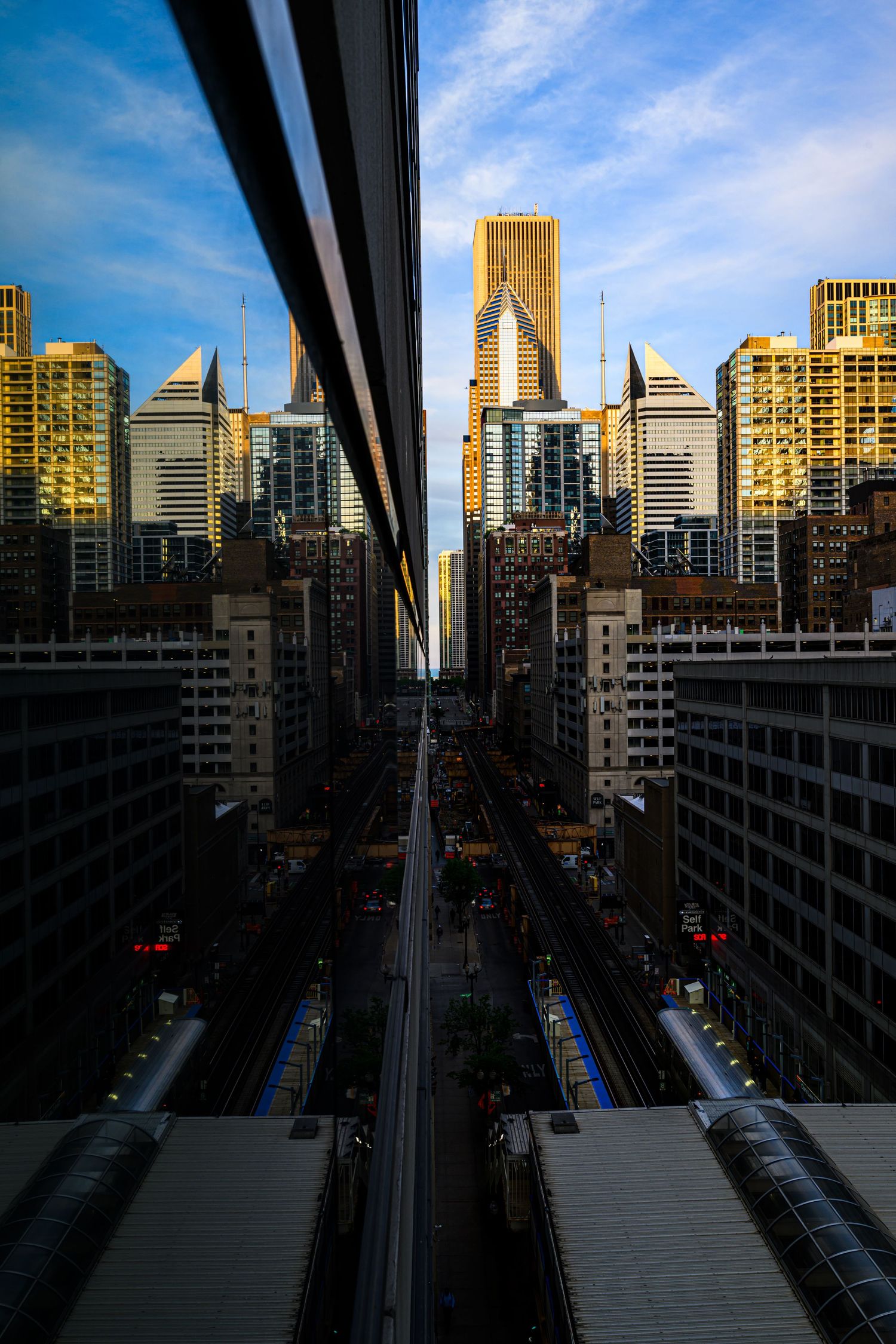 Aerial symmetrical view of Chicago city skyline with skyscrapers, elevated train tracks, and blue sky at golden hour.