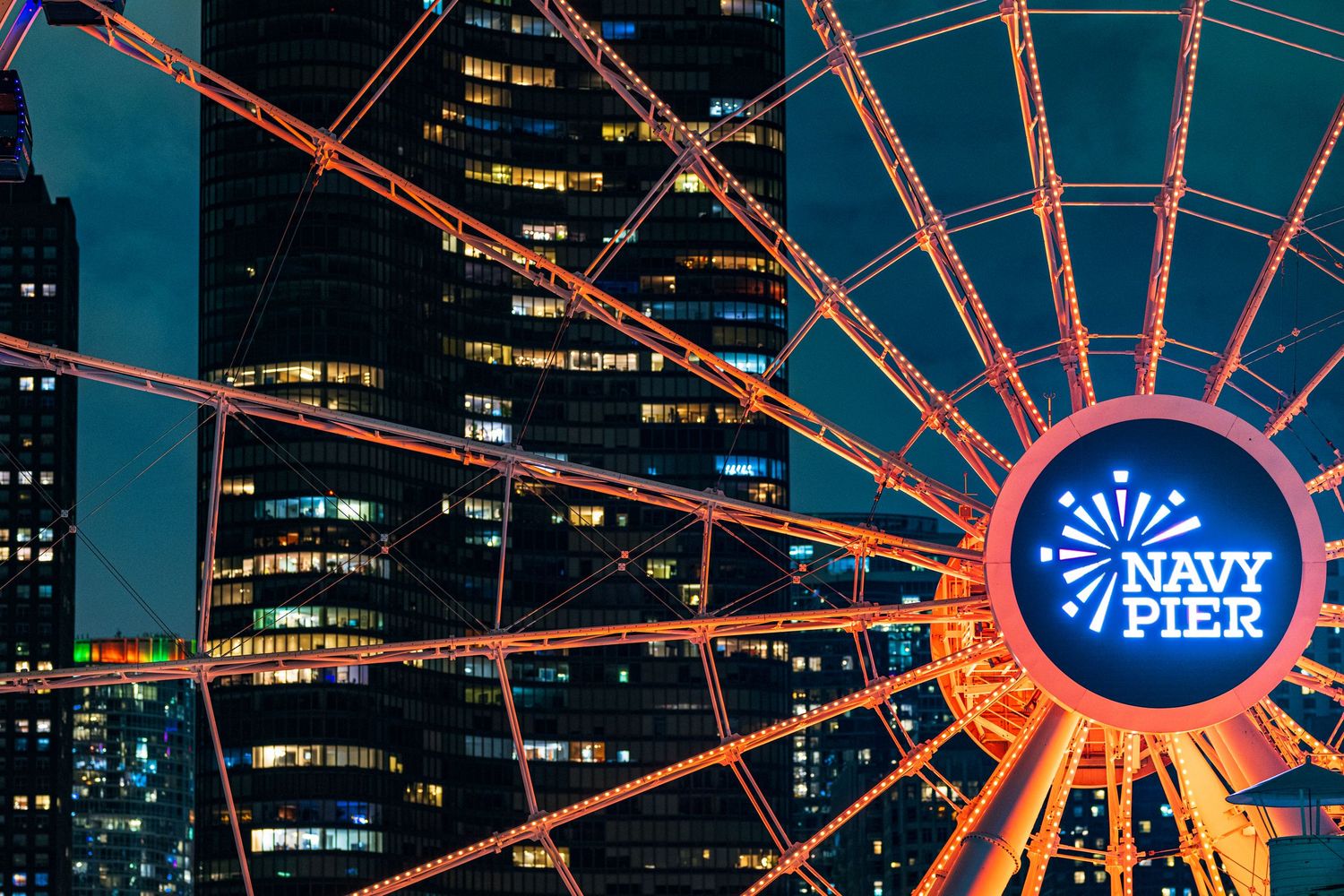 Illuminated Navy Pier Ferris wheel glowing orange at night with Chicago skyscrapers in the background.