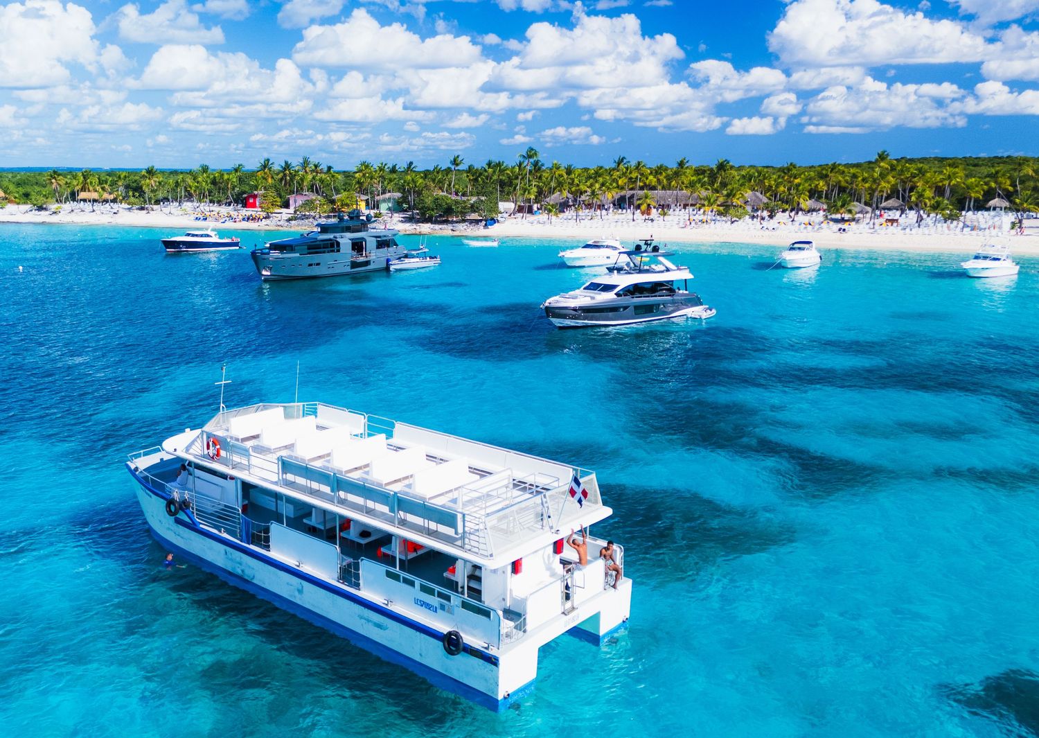 Luxury catamarans and yachts anchored in crystal-clear turquoise waters near a tropical island beach.