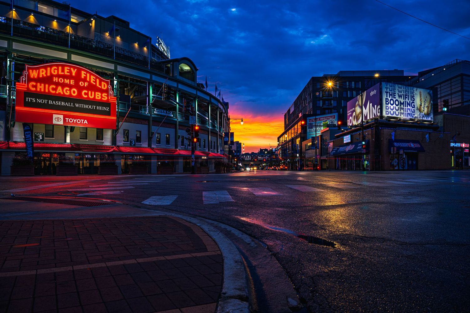 Wrigley Field Chicago Cubs stadium glows at sunset with vibrant orange sky reflecting on wet streets.