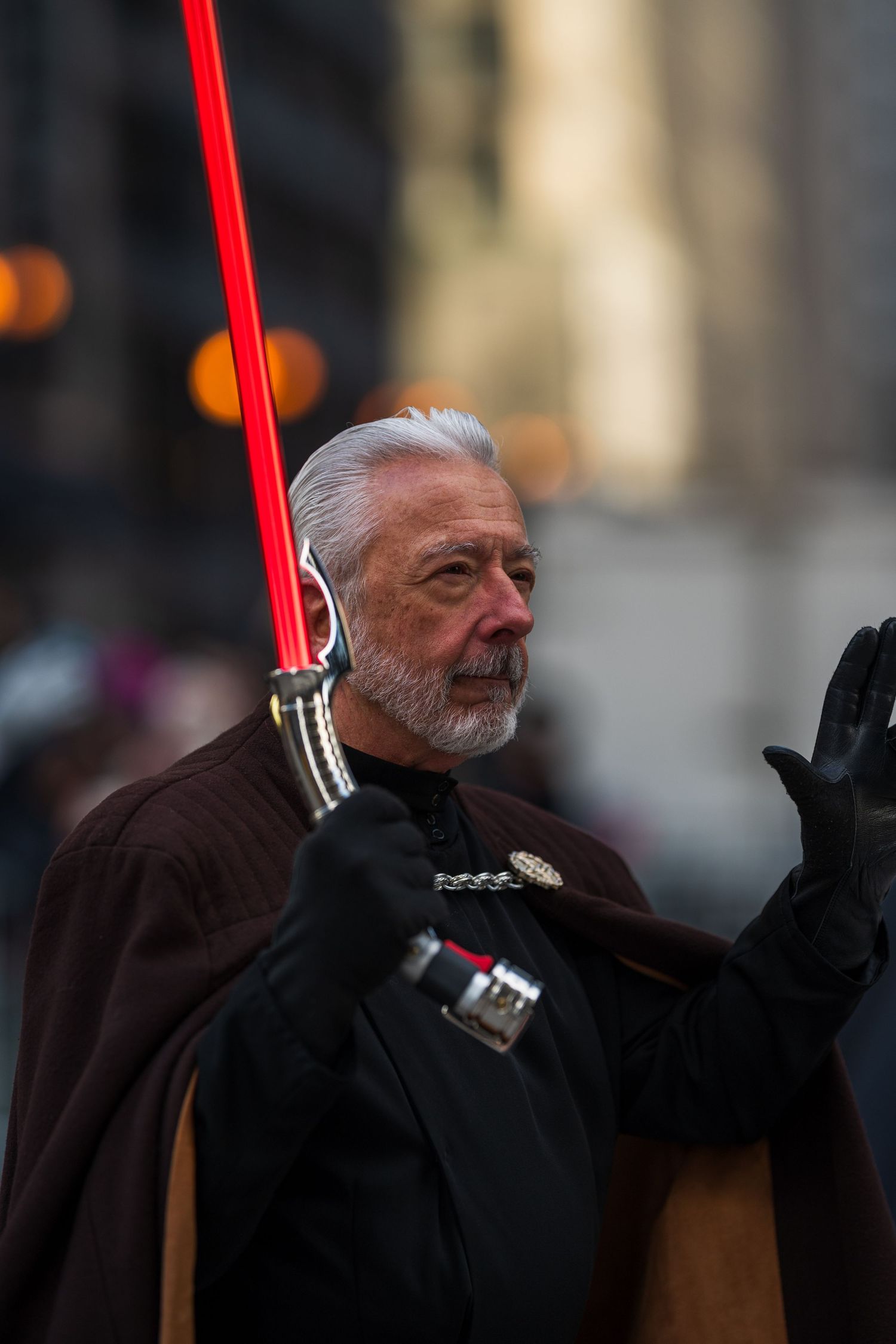 Elderly man in dark Sith costume holding red lightsaber at Star Wars cosplay parade event.