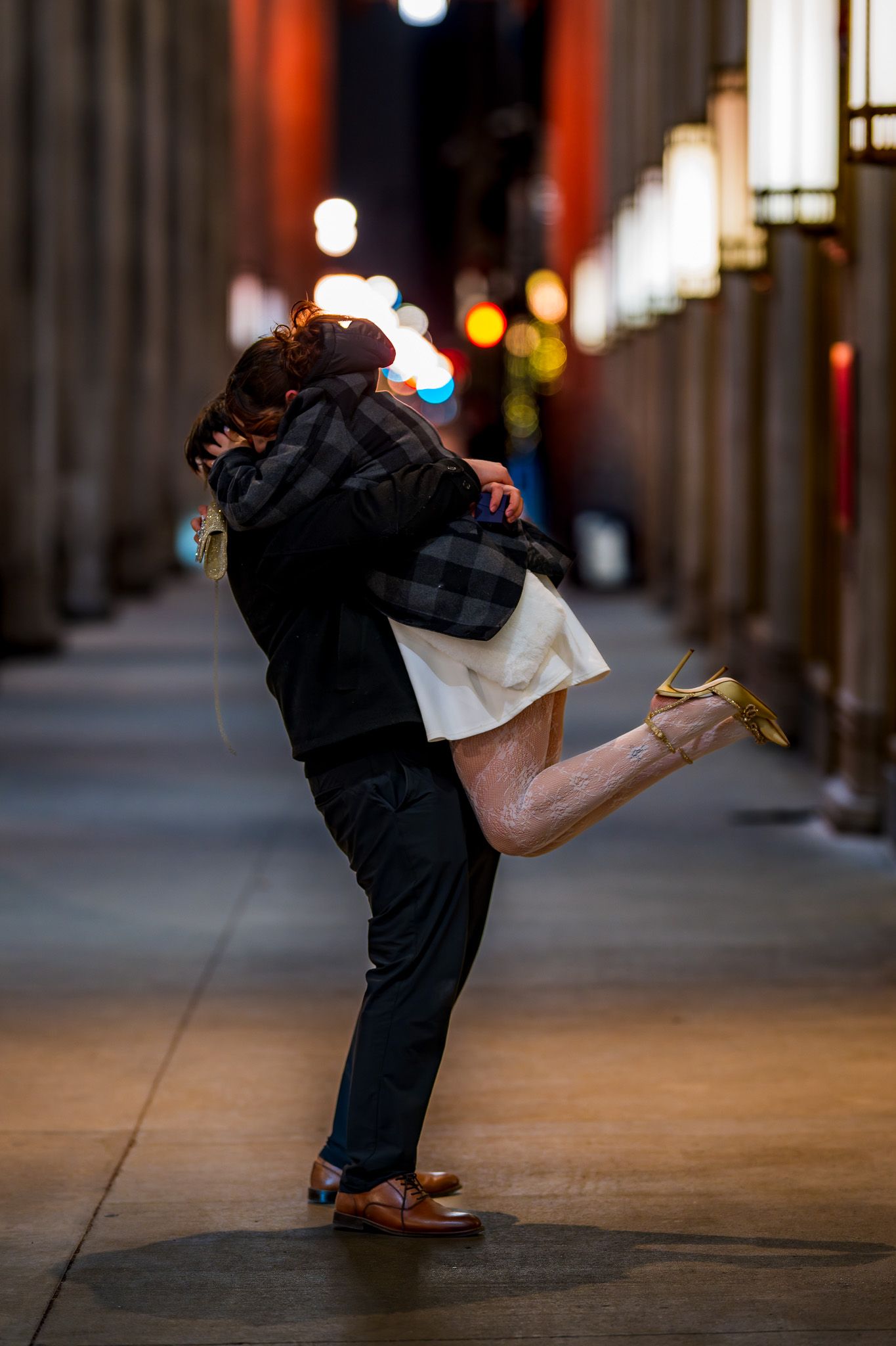 Couple sharing a romantic kiss in a dimly lit urban alleyway at night, woman lifted off her feet.
