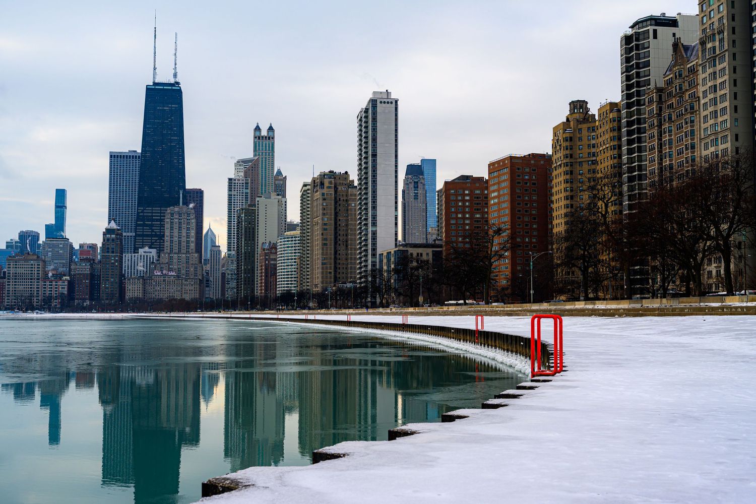 Chicago skyline in winter with snow-covered shoreline, frozen Lake Michigan, and iconic skyscrapers reflected in icy water.