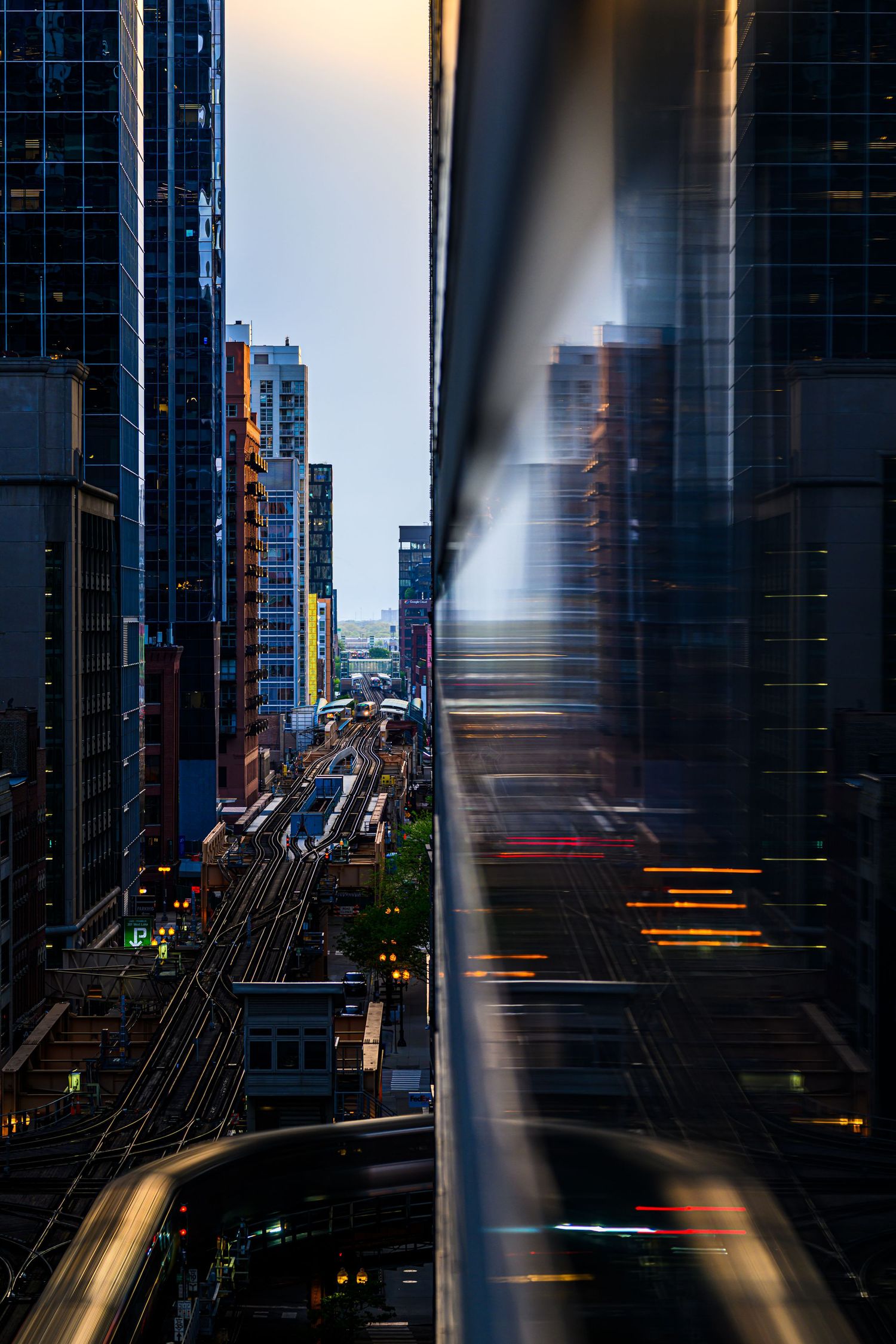 Aerial view of city skyscrapers and elevated train tracks at dusk with light trails and motion blur effects.