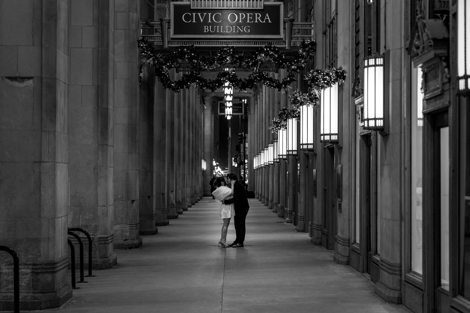 Couple embracing in the grand arcade of Chicago's Civic Opera Building at night in black and white.