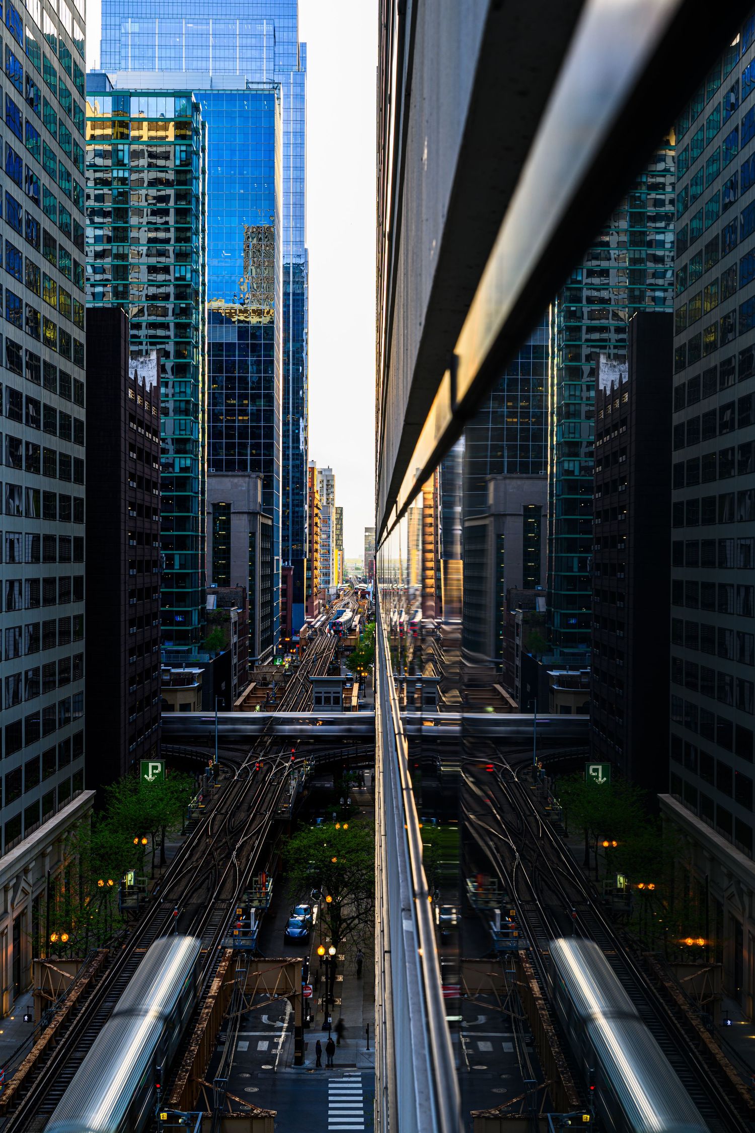 Aerial view of Chicago elevated train tracks between glass skyscrapers at golden hour sunset.