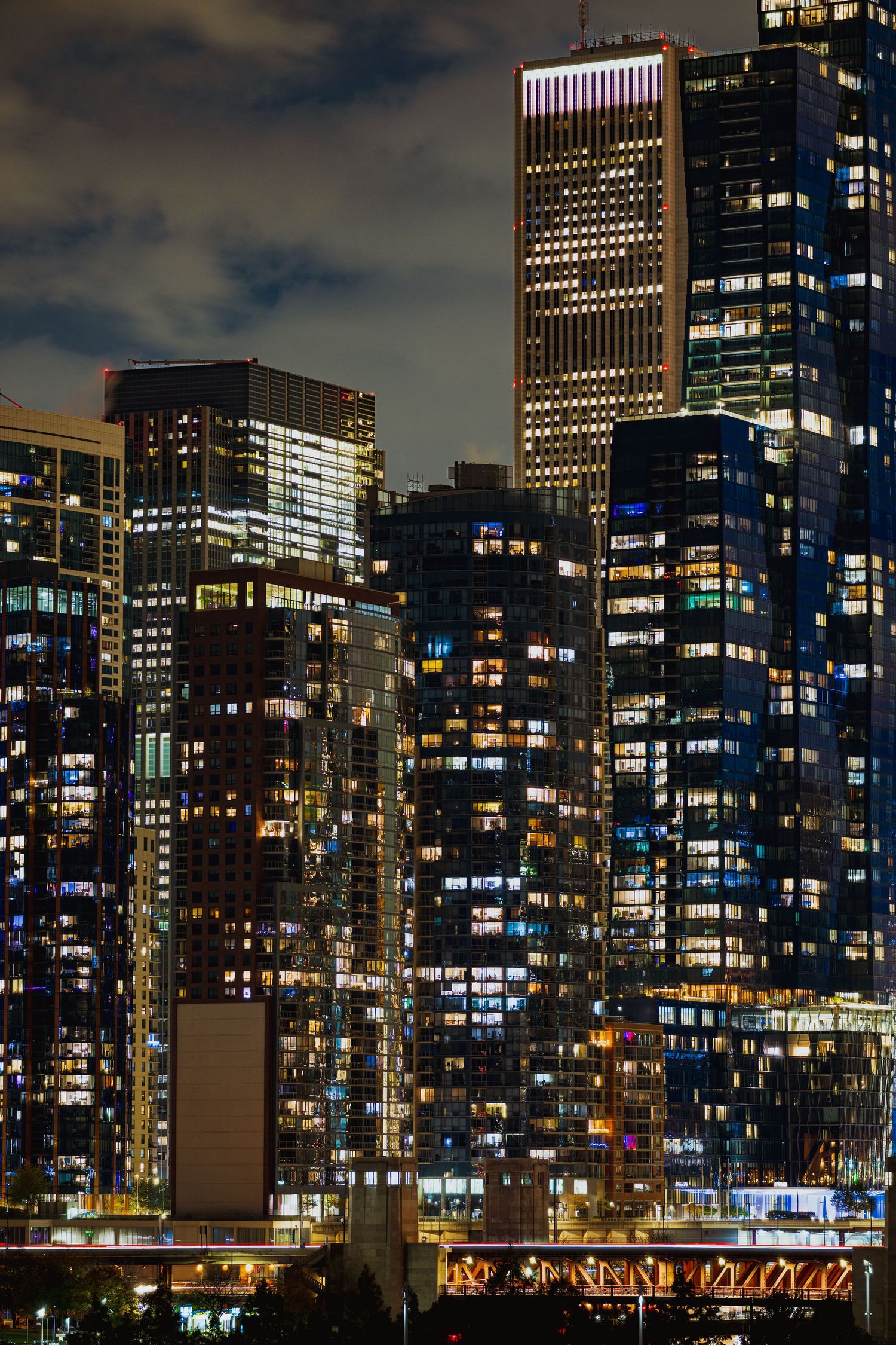 Night cityscape with illuminated skyscrapers and office buildings reflecting colorful lights against a dark sky.