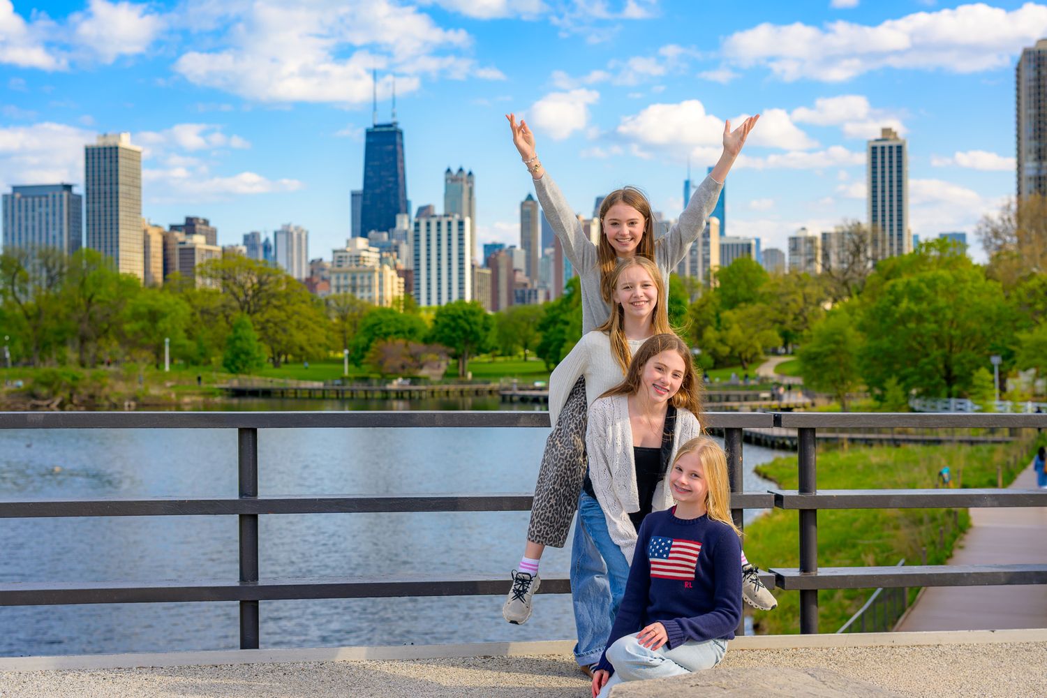 Four girls pose happily on a bridge with Chicago skyline and blue sky in background.